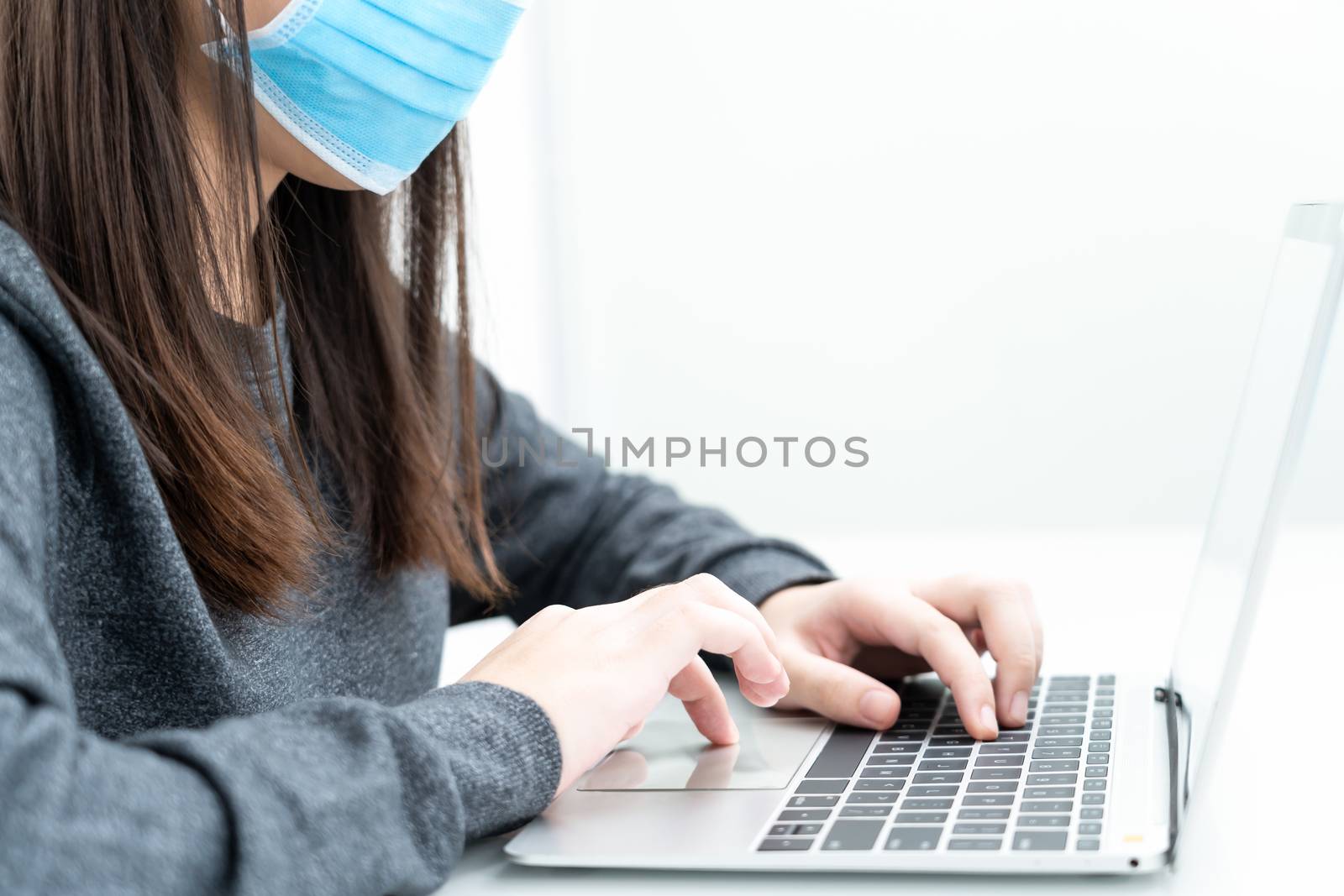 Woman using a laptop computer on the desk at home and wearing protective mask for protection against virus Covid-19