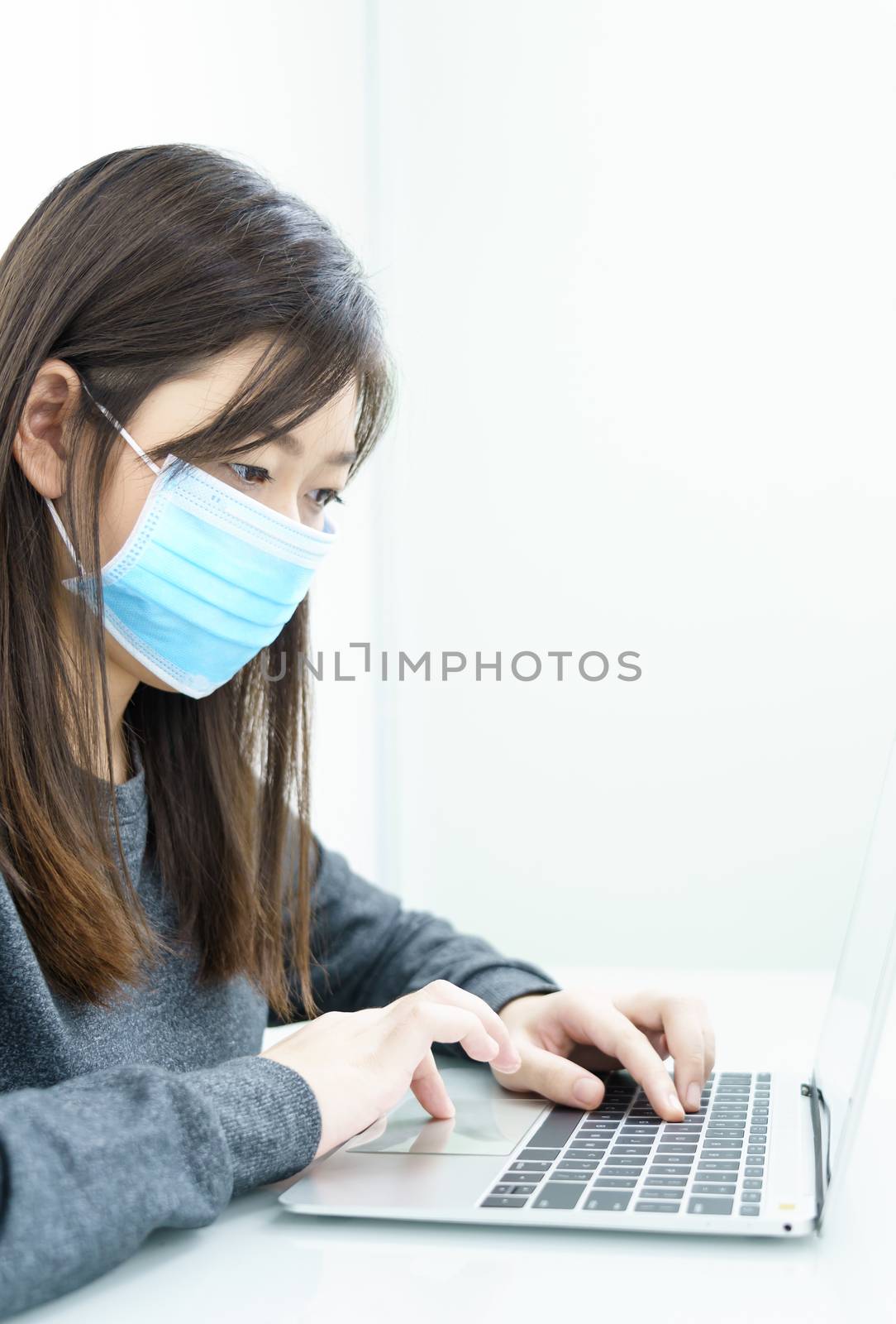 Woman using a laptop computer on the desk at home and wearing protective mask for protection against virus Covid-19