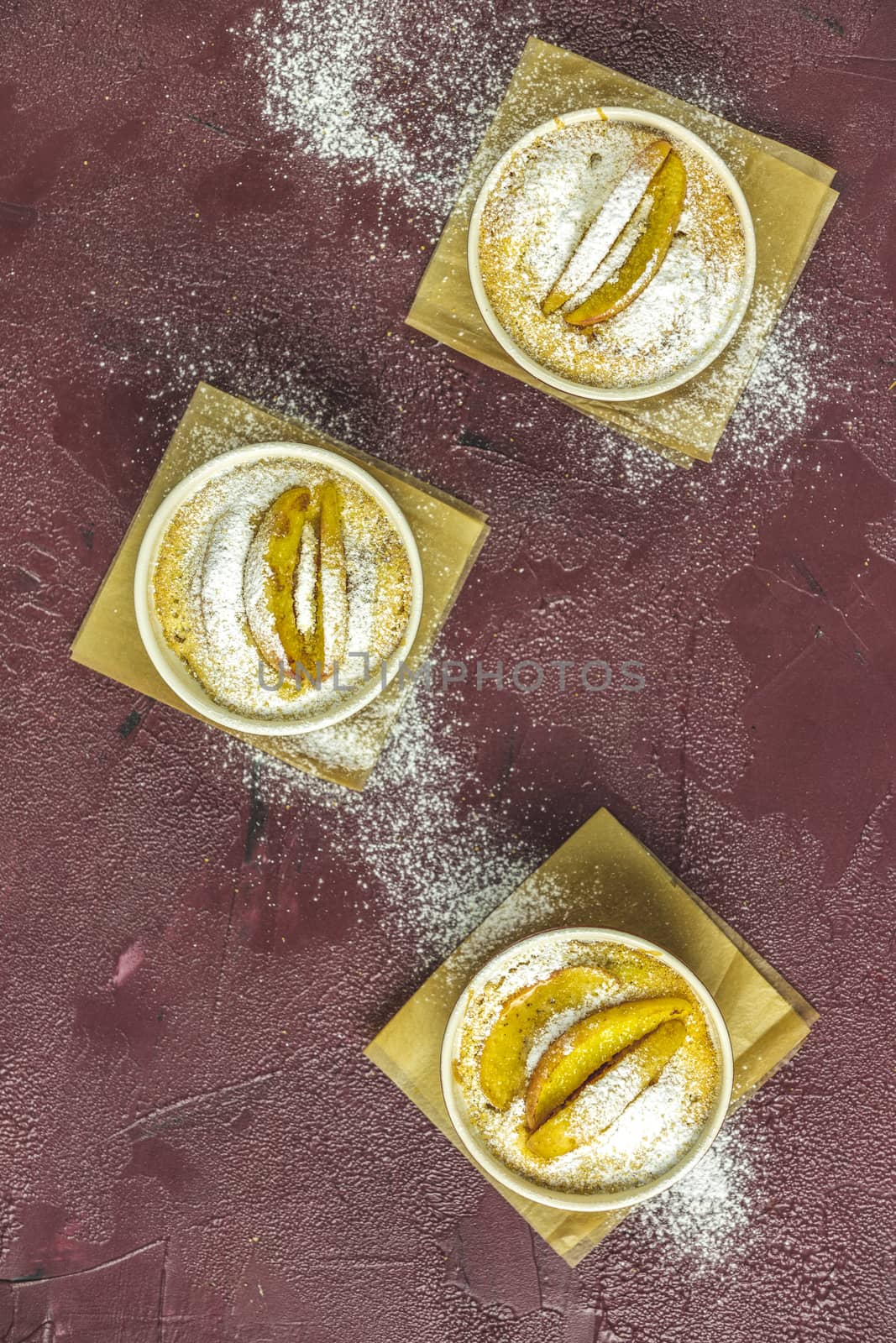 Three apple pies in ceramic baking molds ramekin with parchment  on dark red concrete table. Top view, flat lay.