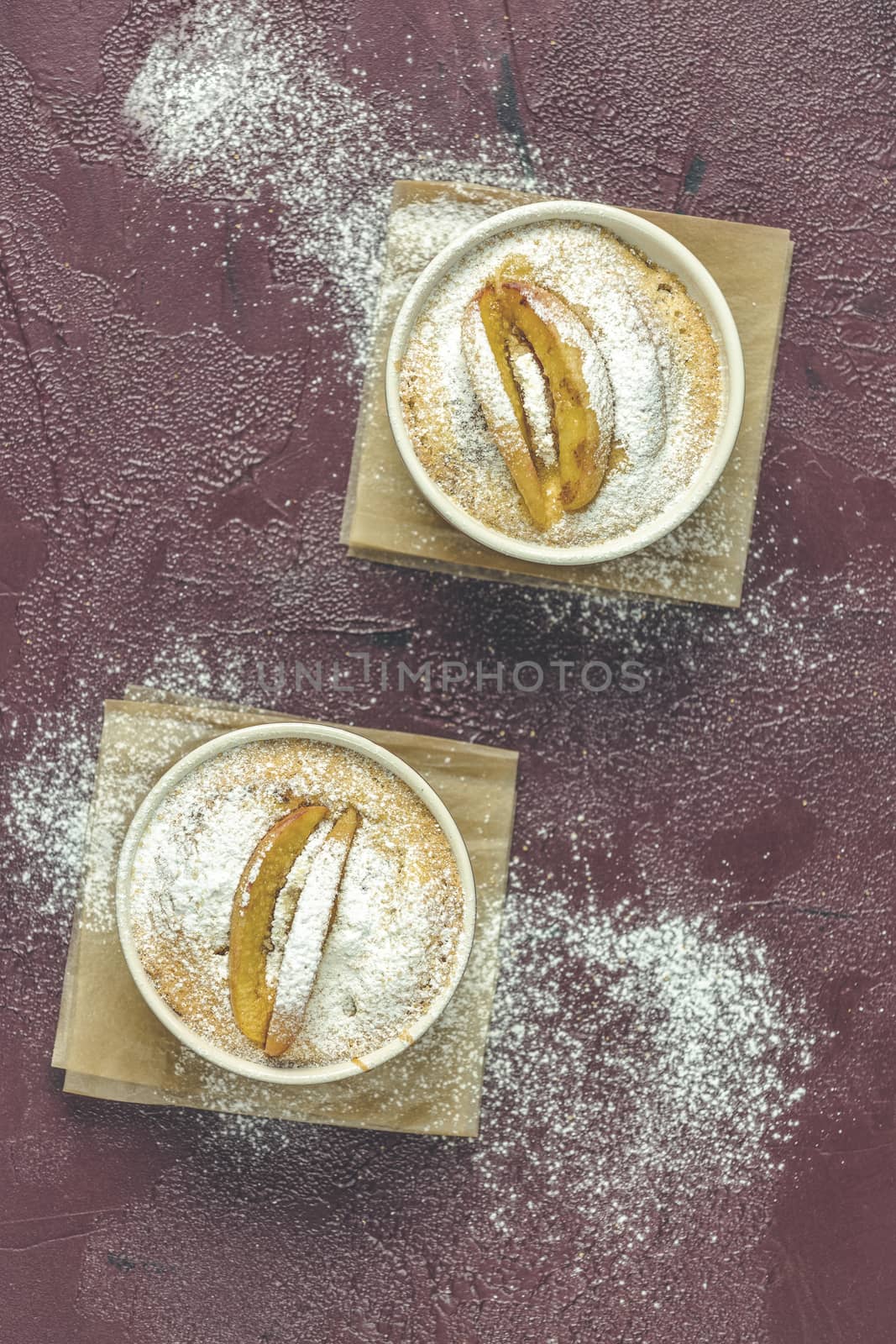 Two apple pies in ceramic baking molds ramekin with parchment  on dark red concrete table. Top view, flat lay.