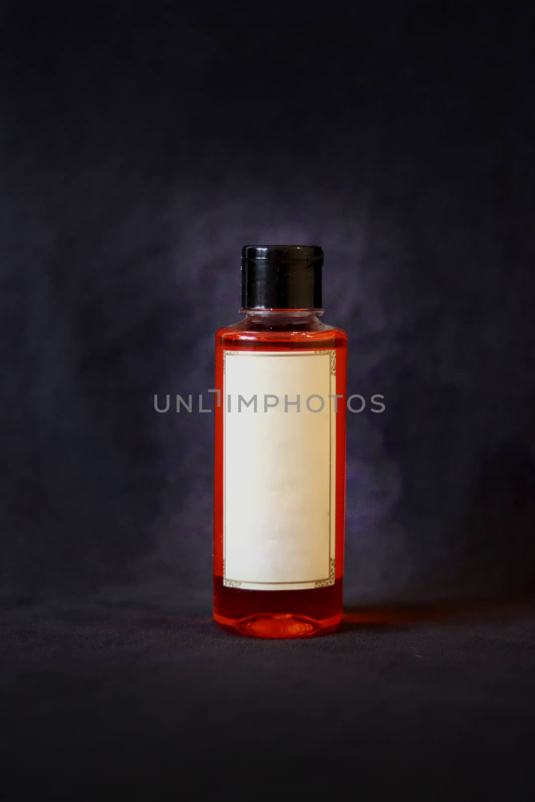 orange oil bottle with off white label and black bottle cap on dark grey textured background.