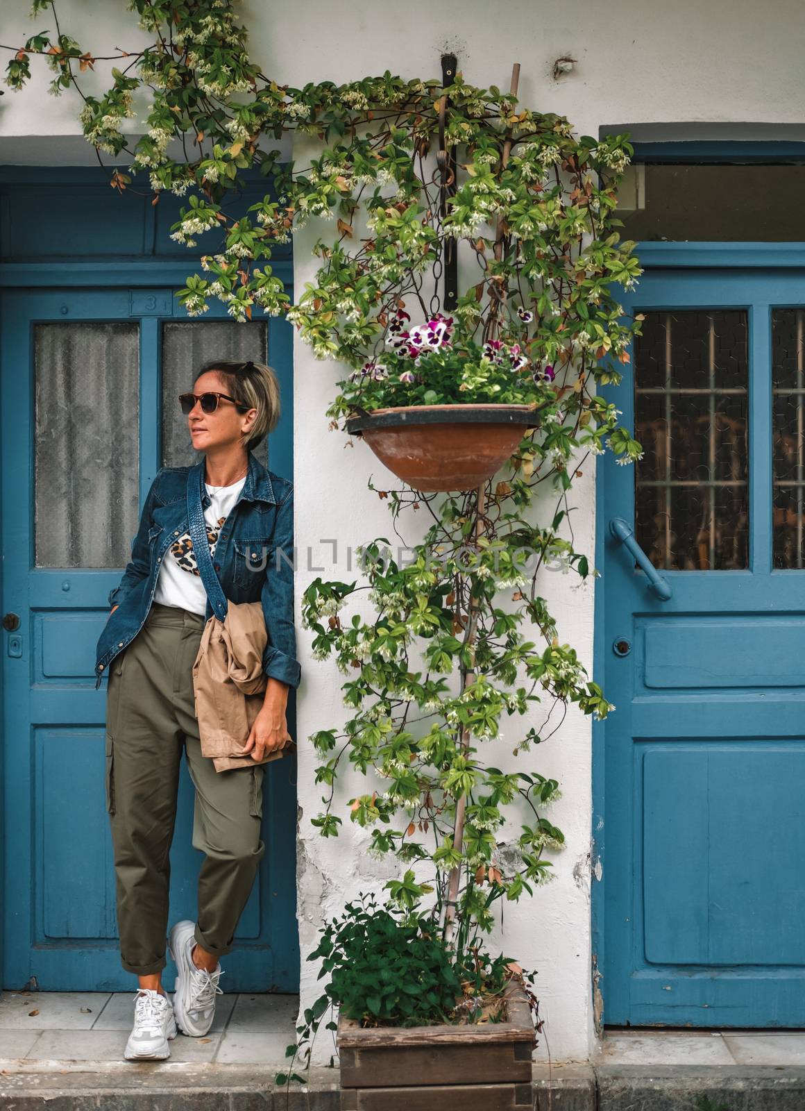 Cool dressed lady in front of turquoise wooden door with flowers around.