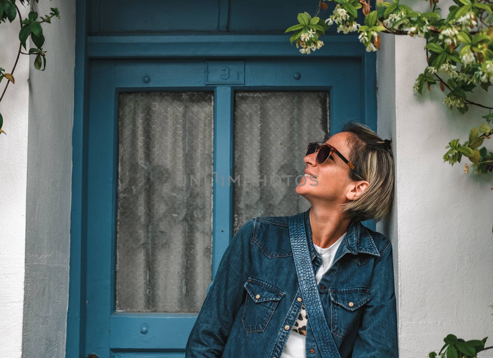 Cool dressed lady in front of turquoise wooden door with flowers around.