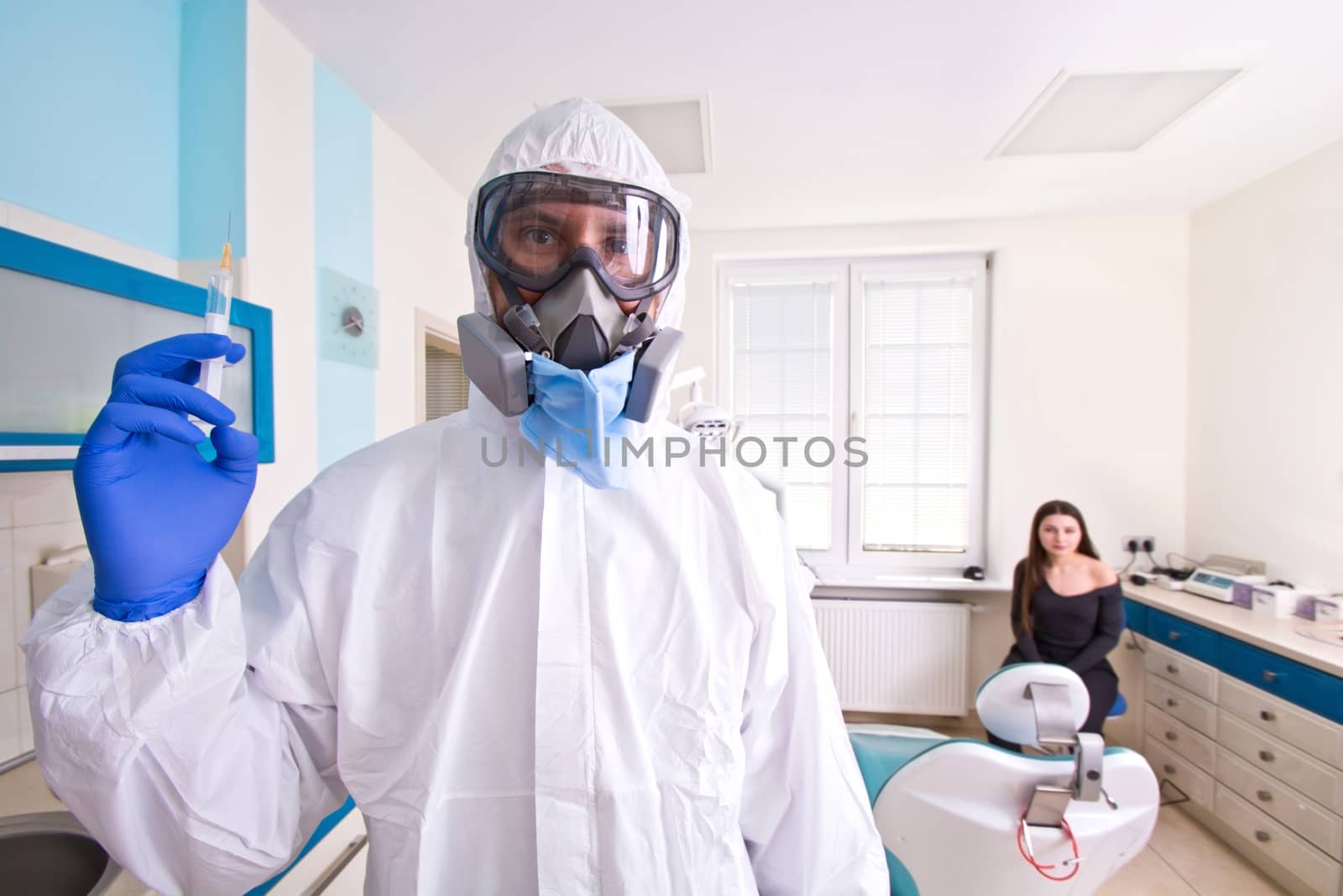 Doctor in protective suit uniform and mask holds injection syringe with vaccine. Female patient waiting for a vaccine. Coronavirus outbreak. Covid-19 concept.