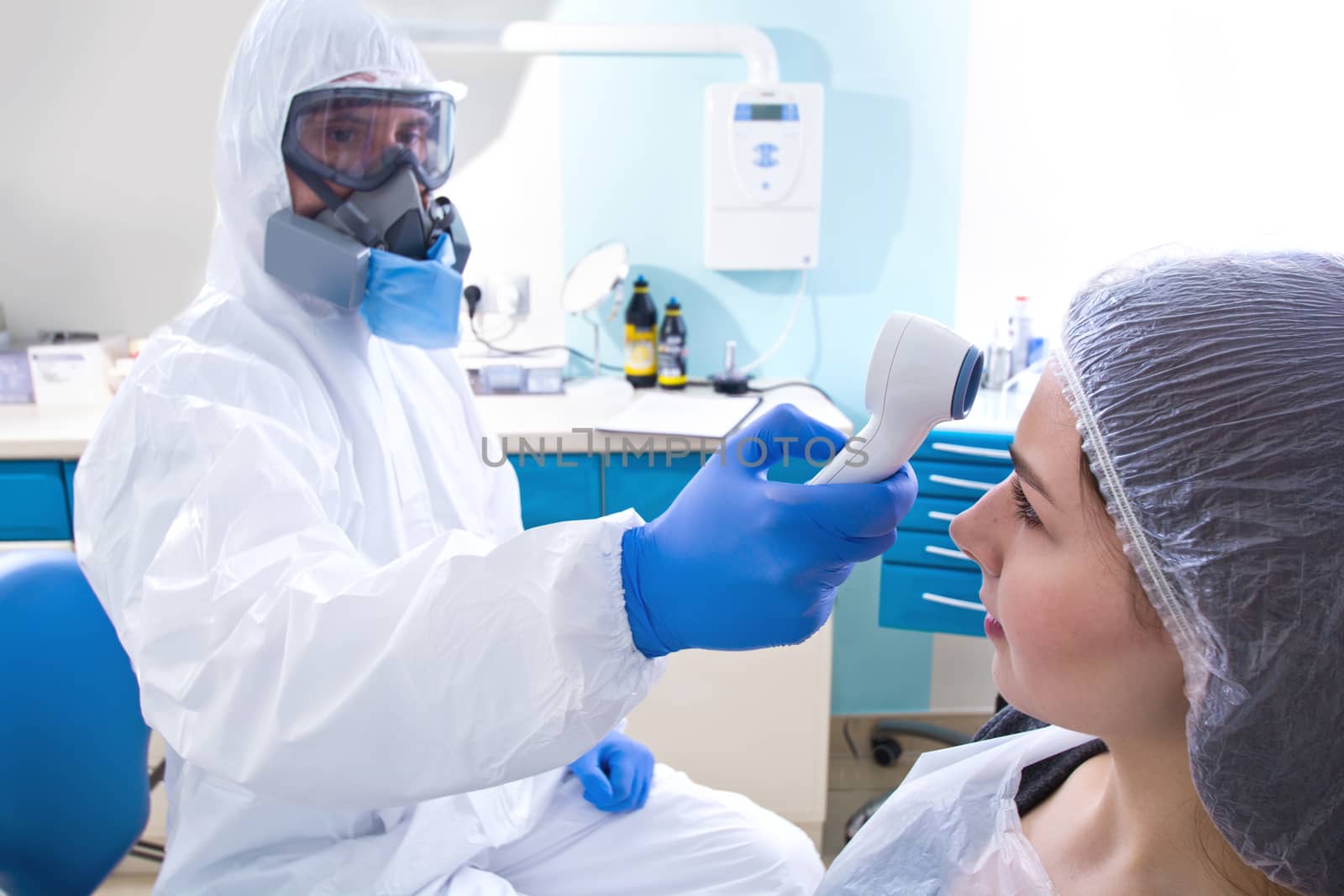 Doctor in protective suit uniform and mask checking temperature of young female patient. by satariel