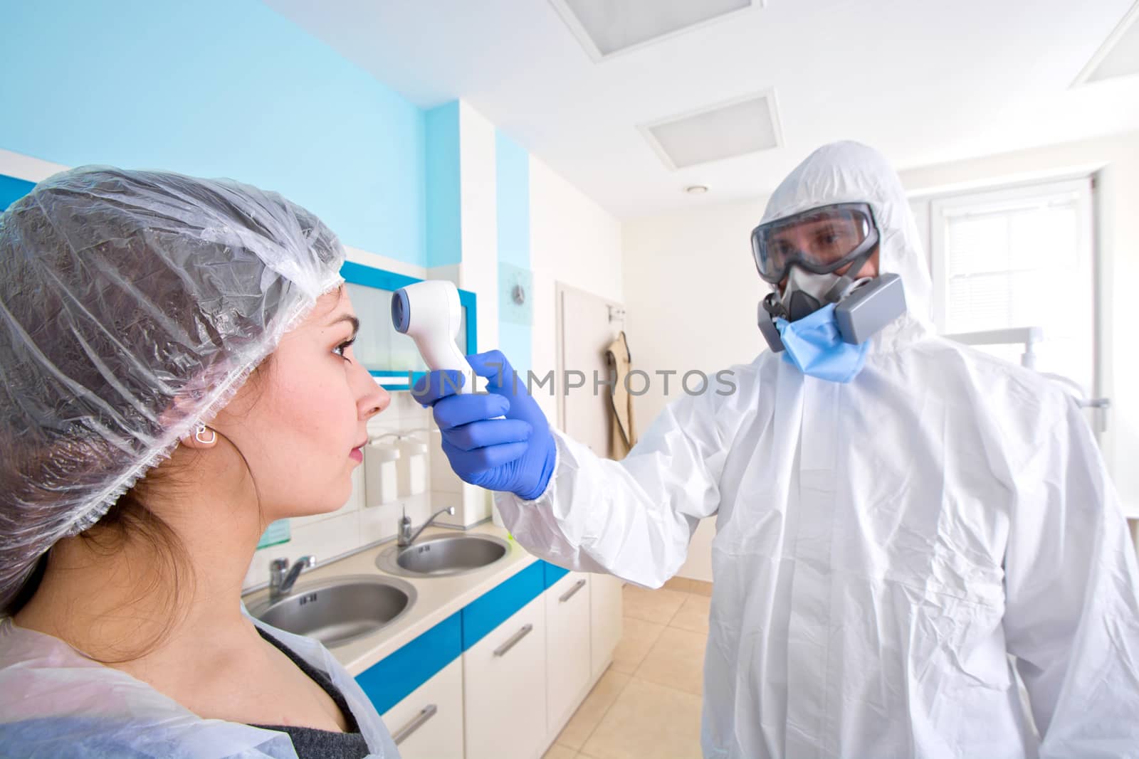 Doctor in protective suit uniform and mask checking temperature of young female patient. by satariel