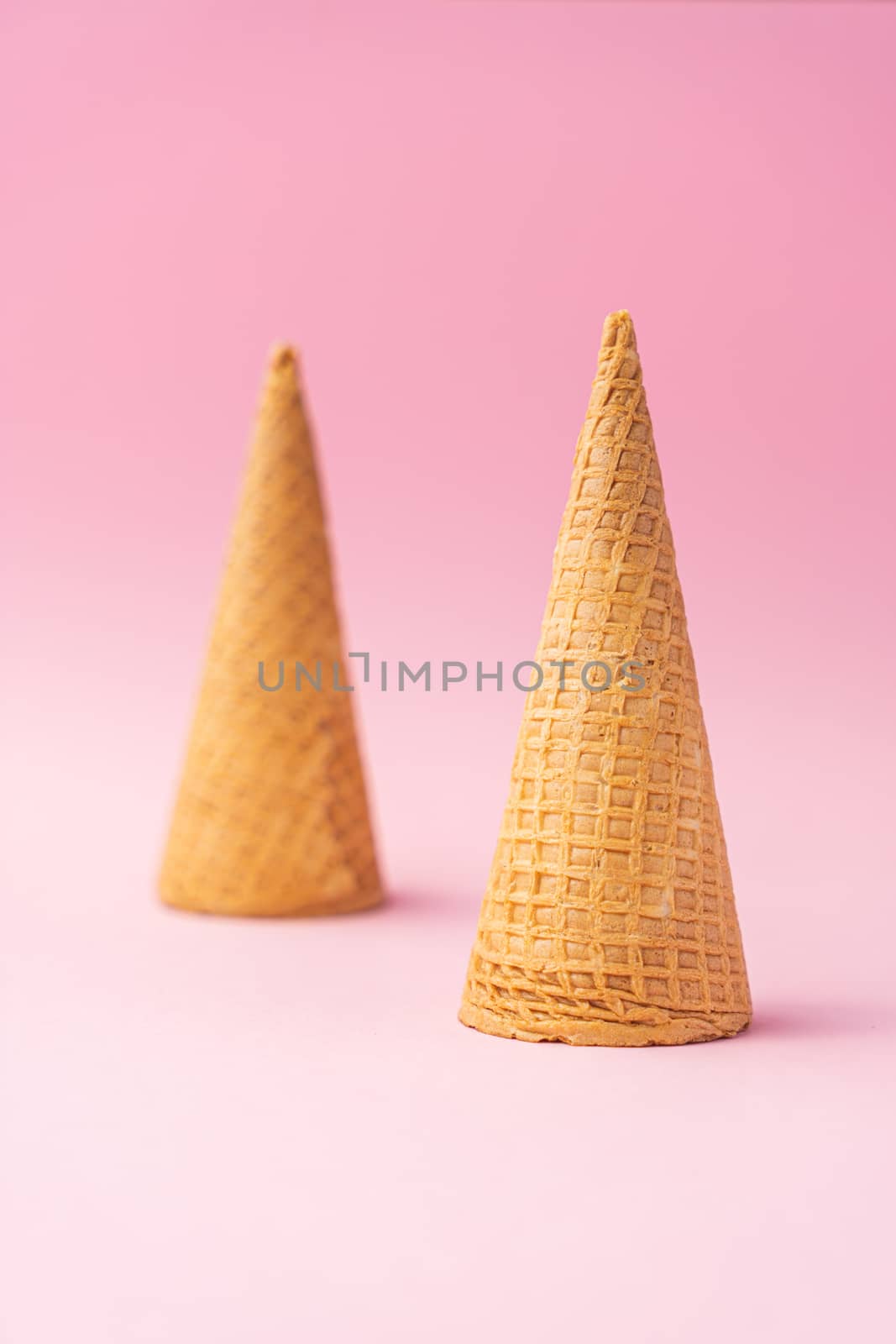 Two upside down wheat flour ice cream cones one in the foreground and the other in the background on a pink background. Summer concept.