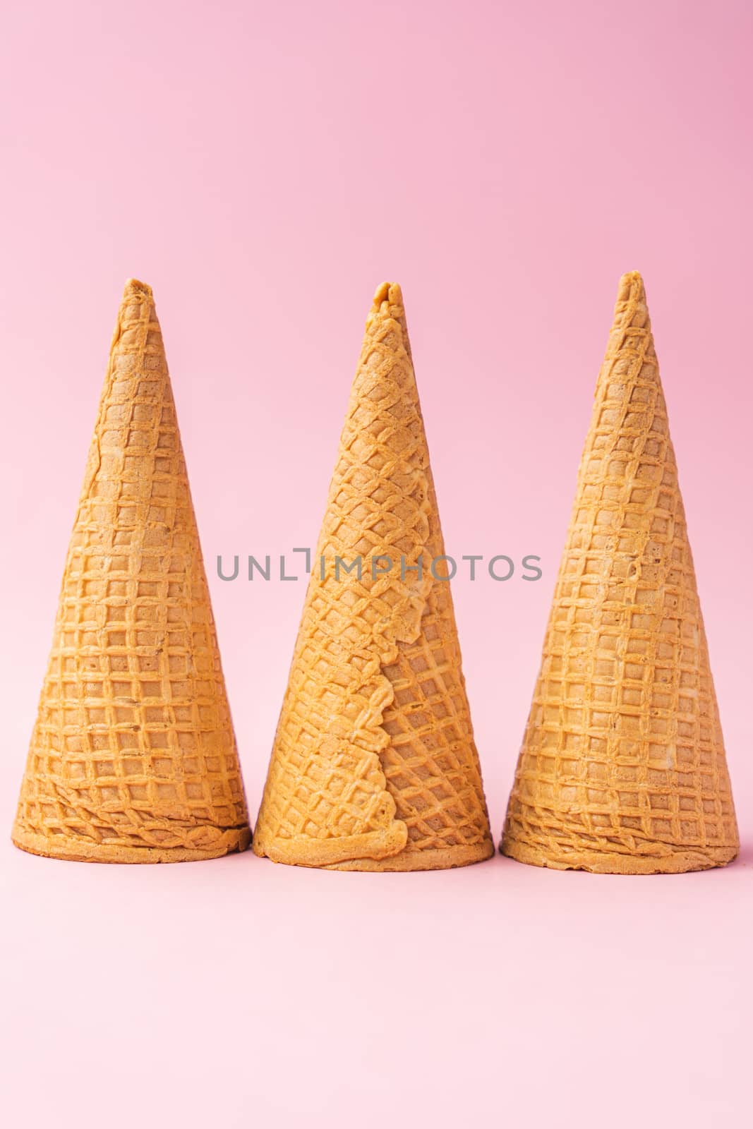 Three upside down wheat flour ice cream cones lined up towards the bottom on a pink background. Summer concept