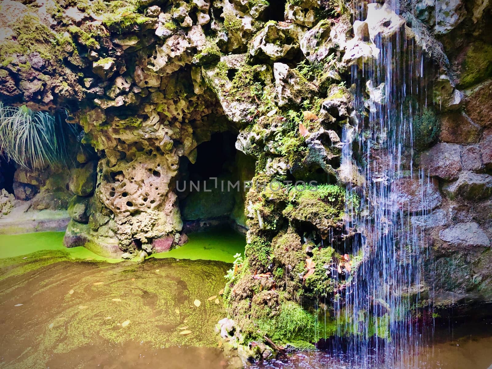 Waterfall in a swamp and caves in the rocks in a bright day
