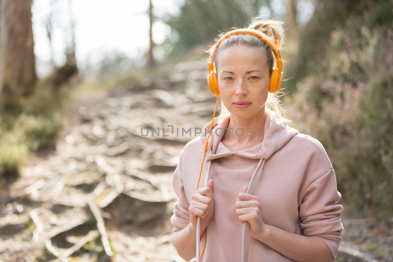 Portrait of beautiful sports woman with hoodie and headphones during outdoors training session. Healthy lifestyle image of young caucasian woman jogging outside.