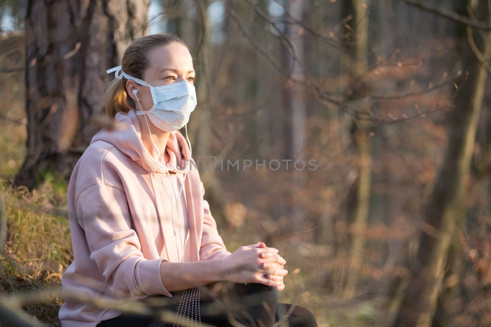 Portrait of caucasian sporty woman wearing medical protection face mask while relaxing in nature and listening to music. Corona virus, or Covid-19, is spreading all over the world.
