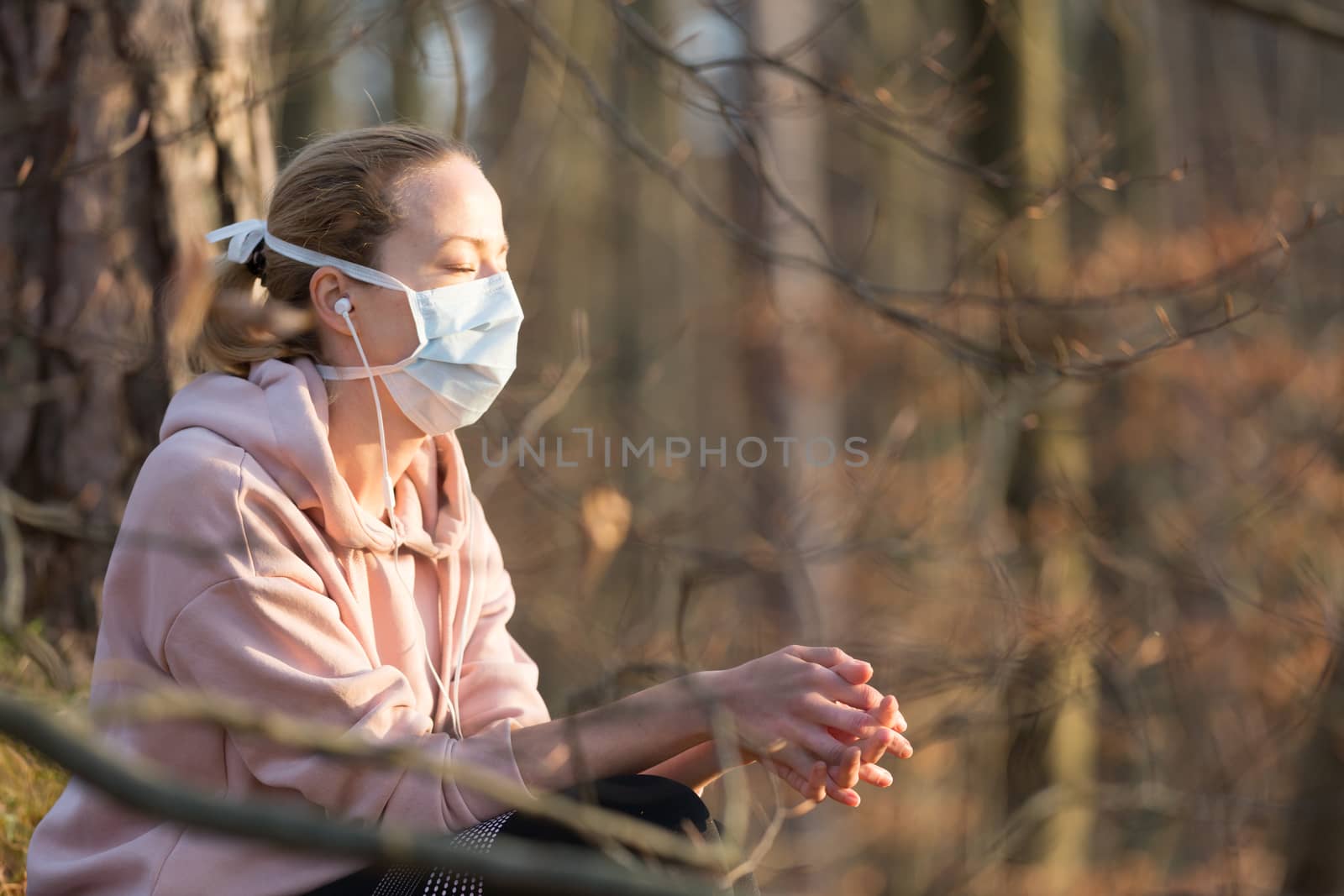 Portrait of caucasian sporty woman wearing medical protection face mask while relaxing in nature and listening to music. Corona virus, or Covid-19, is spreading all over the world.