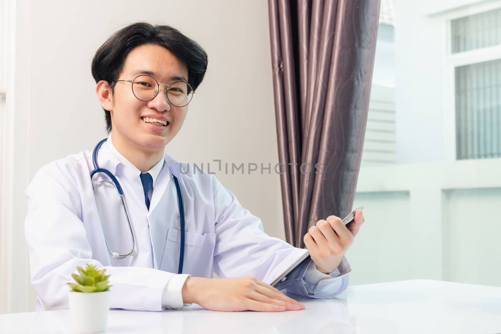 Happy Asian young doctor handsome man smile work from home office wear glasses, using black modern smart digital tablet computer on desk at hospital office, Technology healthcare and medicine concept