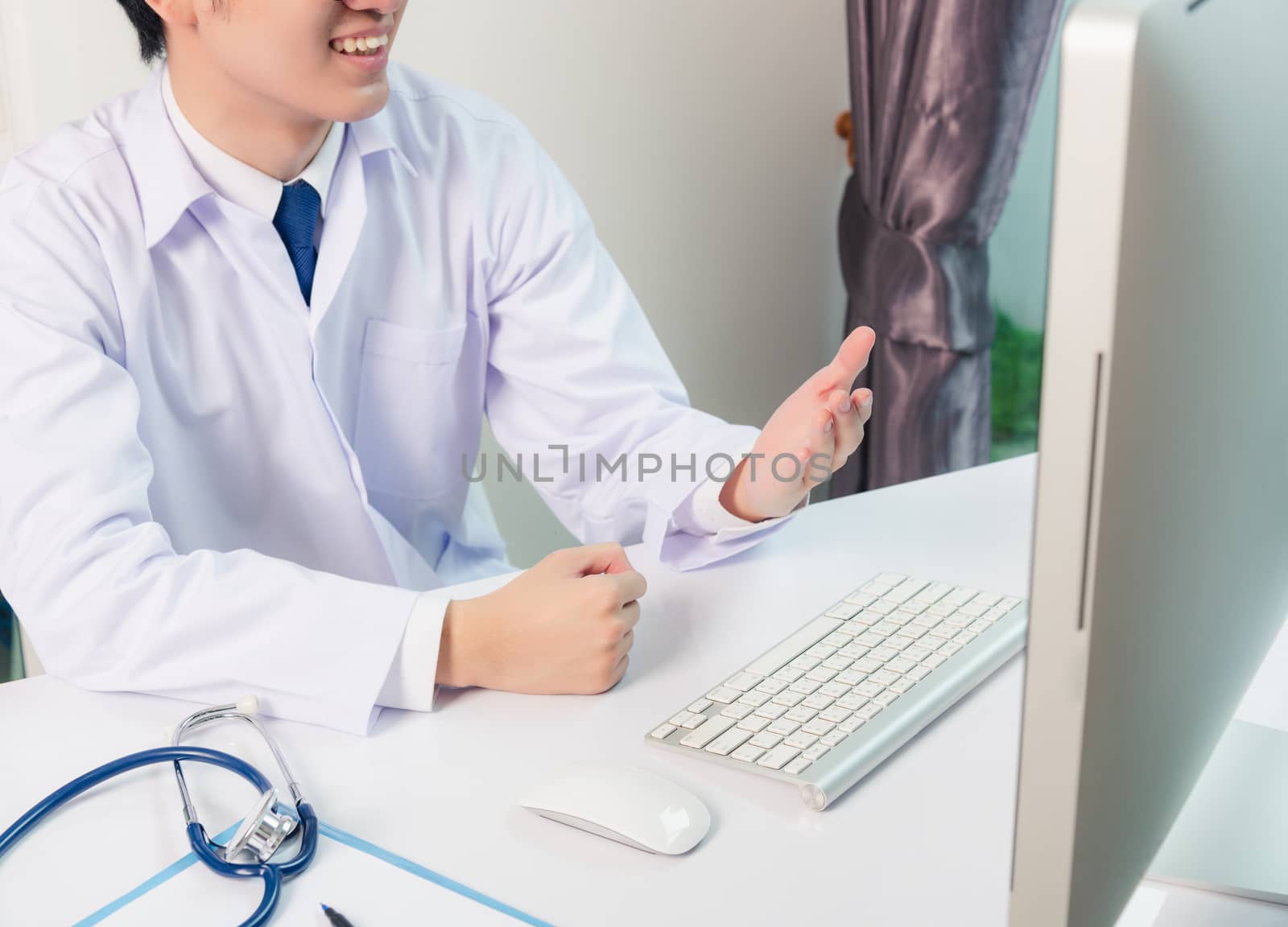 Asian young handsome doctor man wearing a doctor's dress and stethoscope video conference call or facetime raise hand to explain the symptoms he smiling at hospital office, Health medical care concept