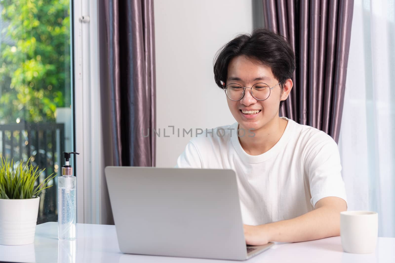 Happy Asian young business handsome man smile work from home office wear glasses and t-shirt comfortable working with laptop computer on desk, Thai person freelance man worker at home