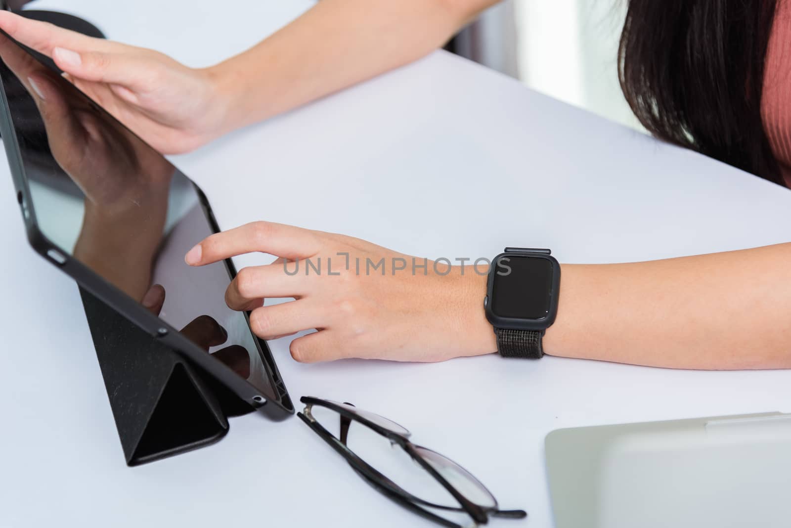 Work from home, Happy Asian young businesswoman use hand finger touch screen modern digital smart tablet computer she wears a smart watch on the wrist focus on smartwatch
