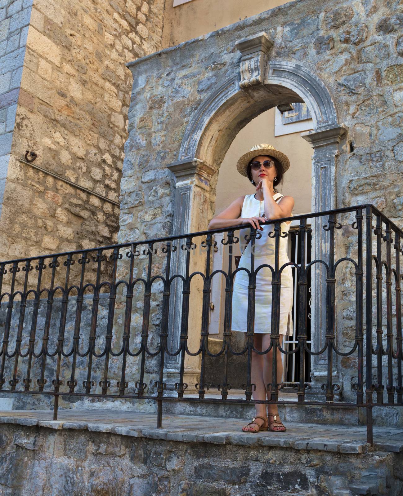 Woman in sun glasses and straw hat. Fashion. A beautiful lady in a straw hat is standing on the porch of an old house against the background of an openwork antique arch.