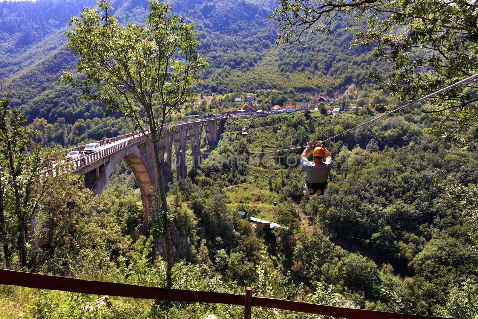 A man crosses over a long cable car over a mountain and forest across the Tiara River in Montenegro near the high stone bridge.