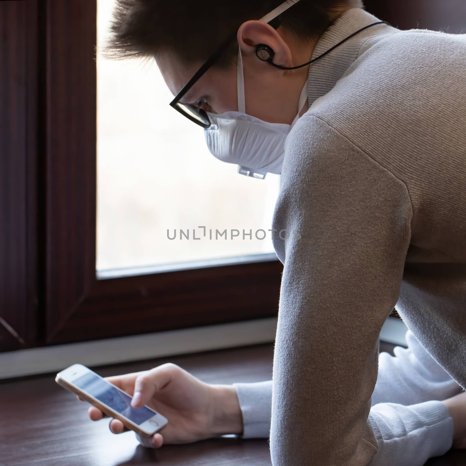 A young man in a medical mask looks at the phone screen for information by bonilook