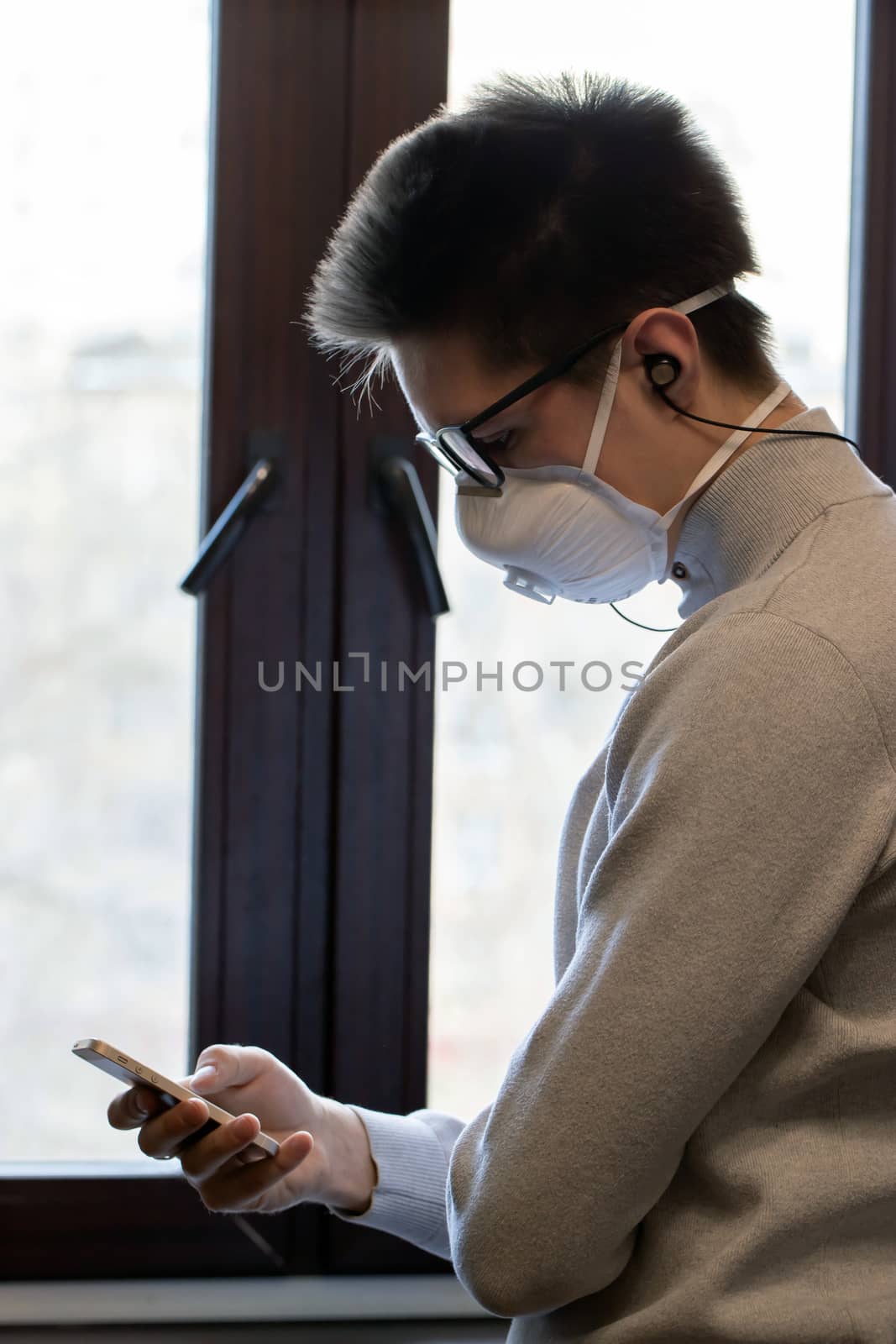 A young man in a medical mask looks at the phone screen for information by bonilook