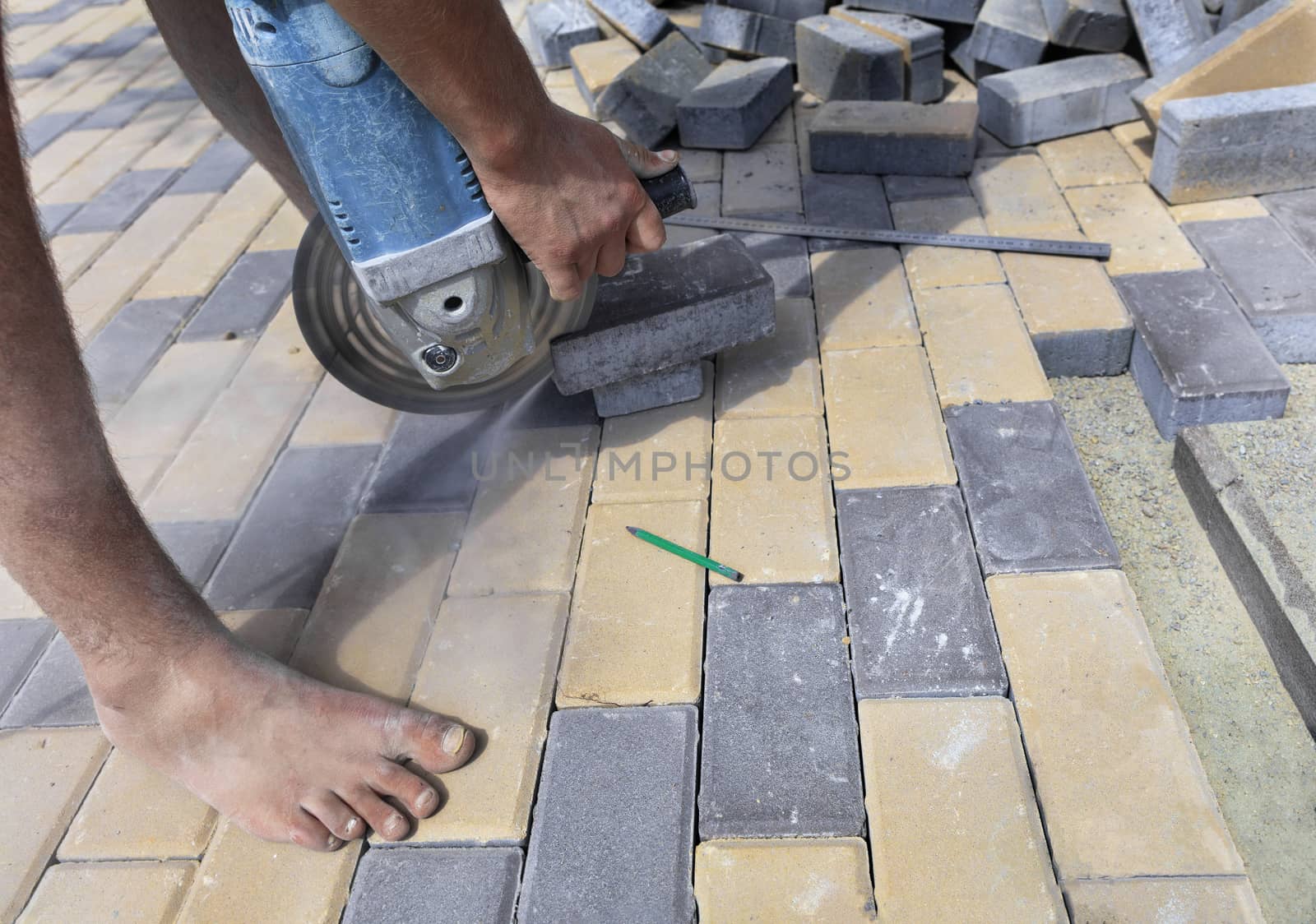 The worker cuts a bar of paving slabs for the final laying on the terrace on a city street at noon.