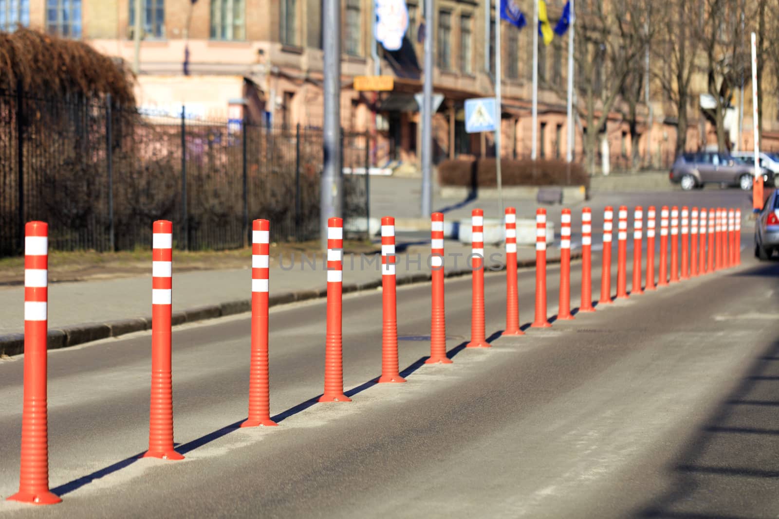 Red reflective road columns divide the road in half against the background of a city street and parking in the light of the sun's rays.