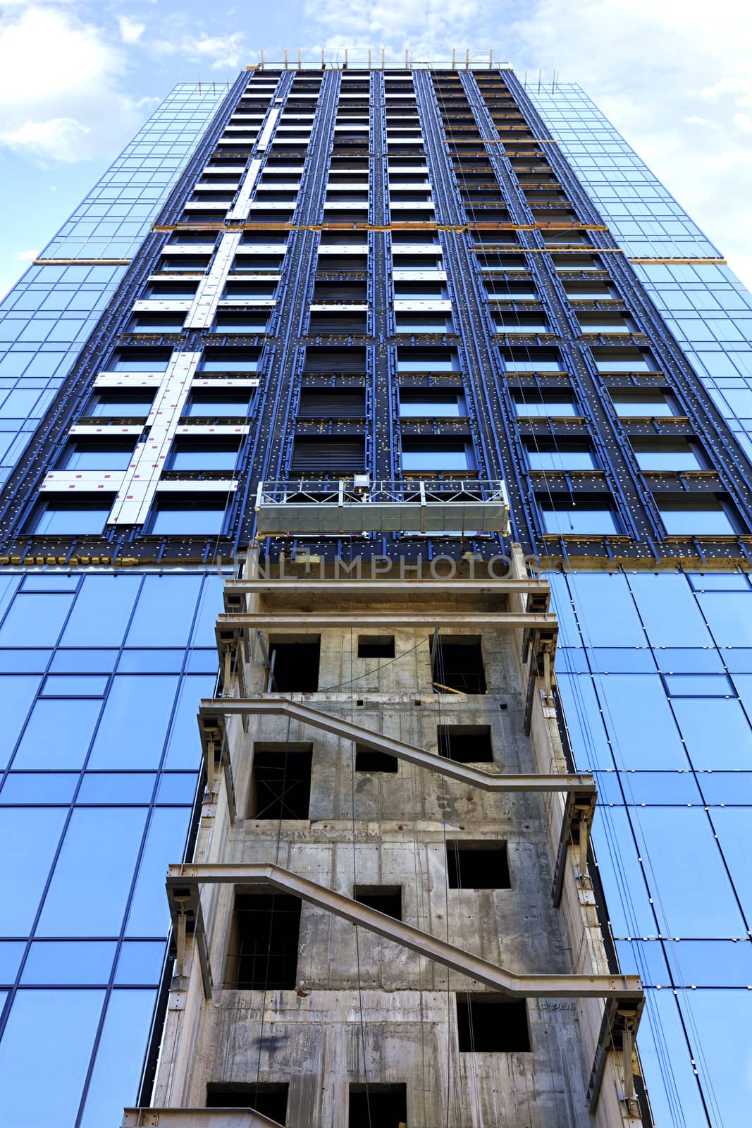 Facade of a modern concrete building under construction glazed from bottom to top against a blue sky with white clouds.