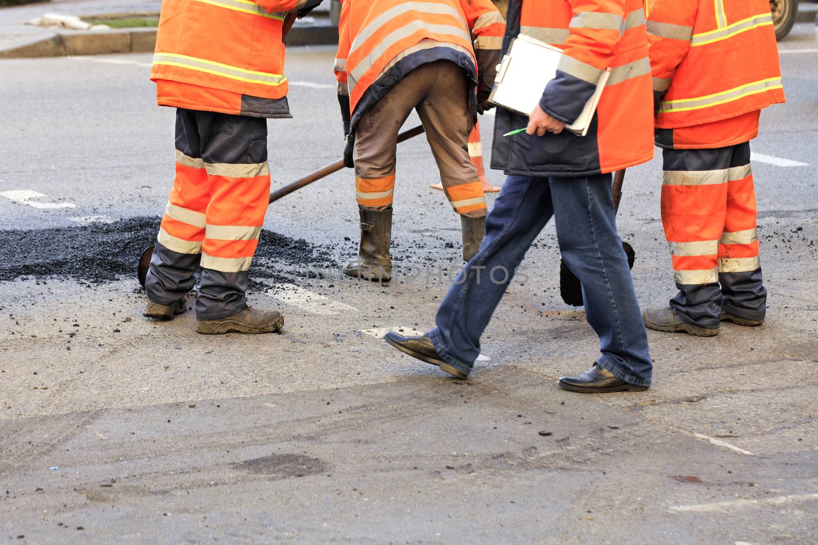 A team of road builders collect and align fresh asphalt with a shovel along the repaired part of the road. by Sergii