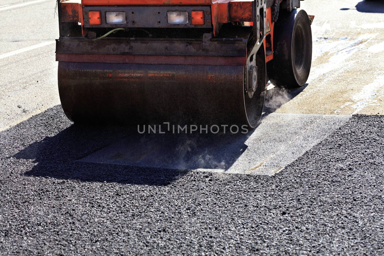 A heavy vibratory road roller compacts asphalt on the repaired stretch of road. by Sergii