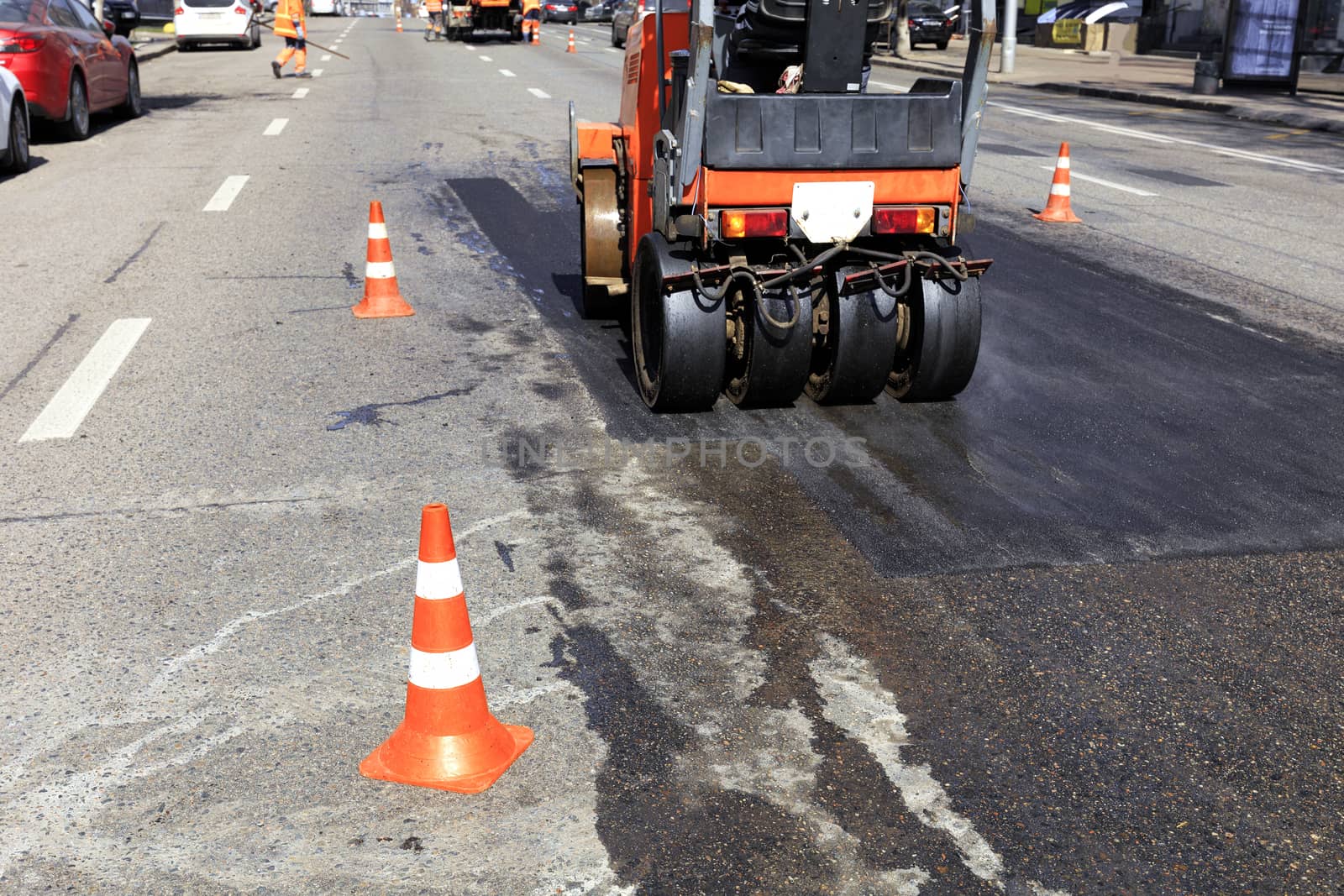 Road red cones enclose a section of the road on a city street for repairing asphalt pavement and work of road roller