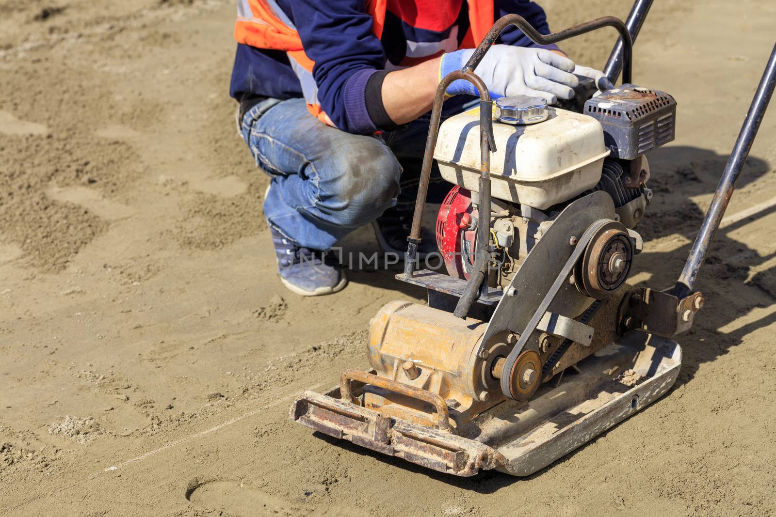 A worker cleans an old gasoline compactor to compact sandy soil. by Sergii