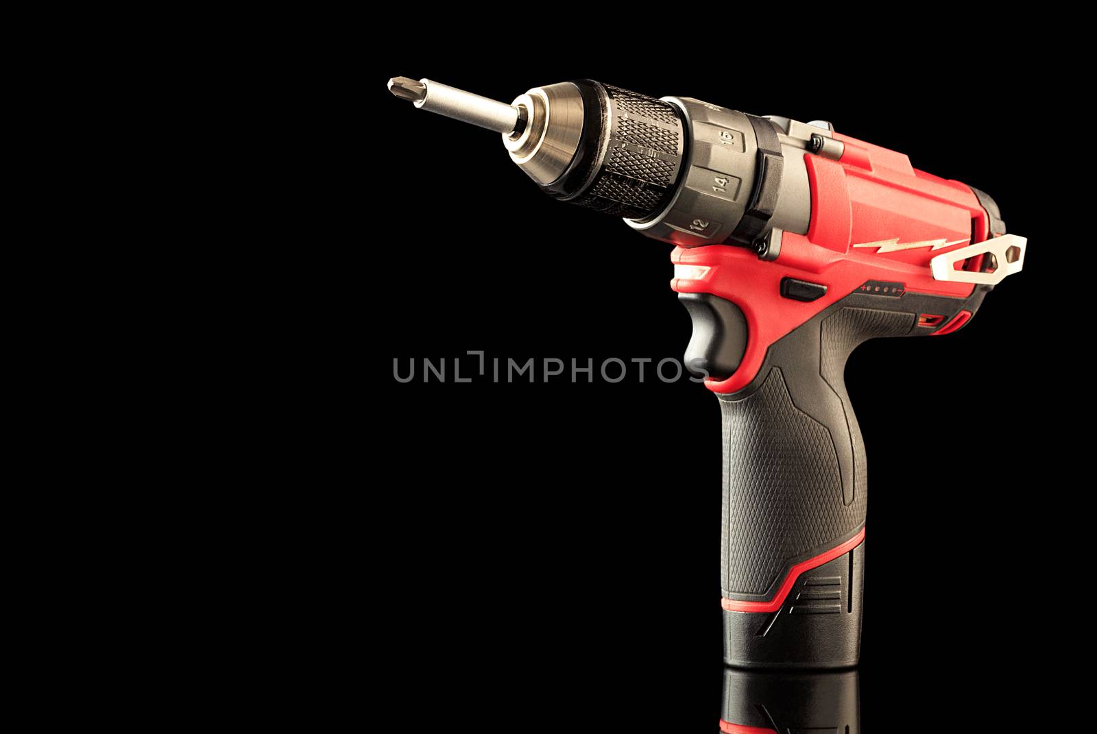 Cordless drill screwdriver red with rubberized grip isolated on a black background with reflection