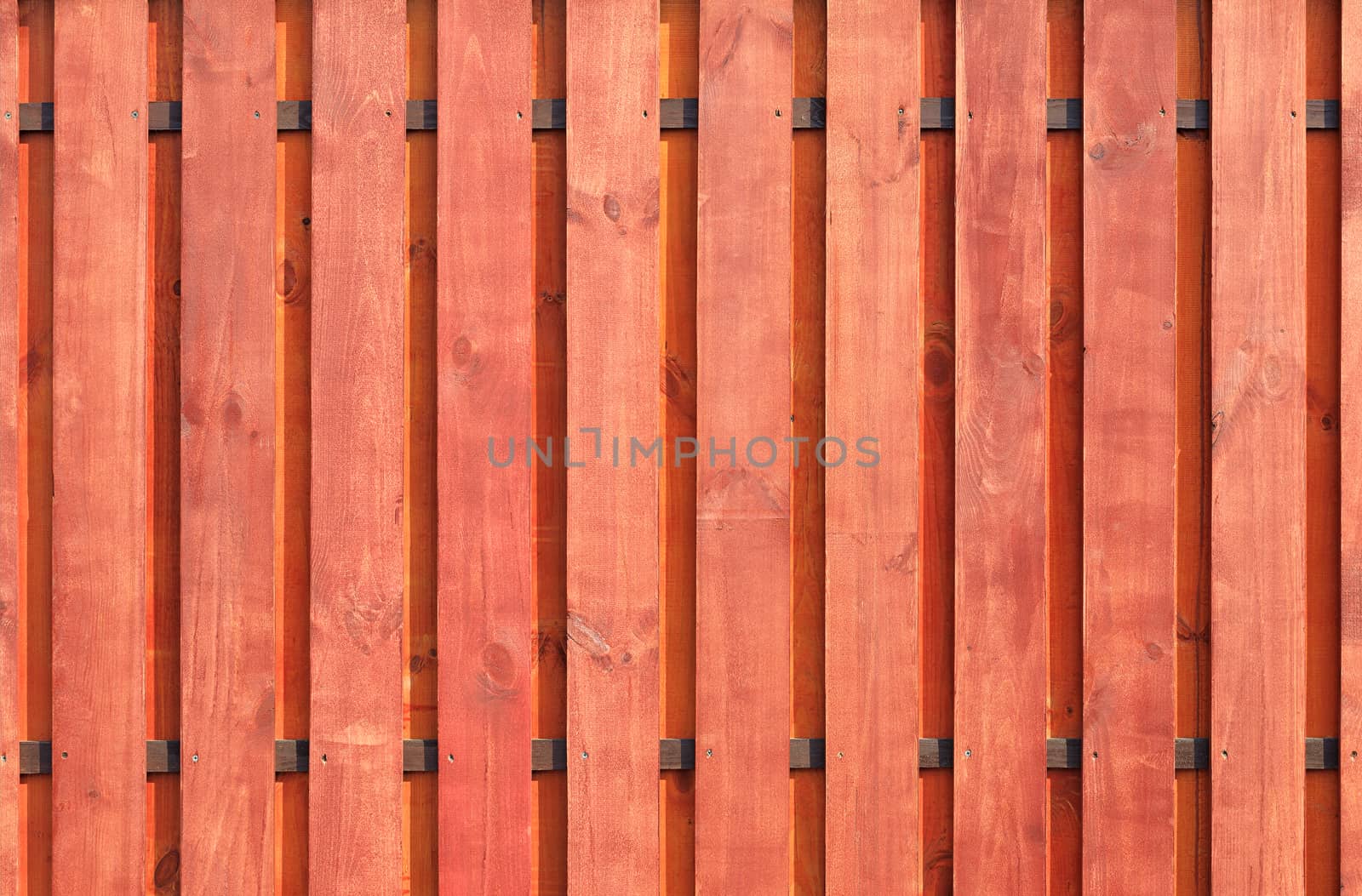 A new vertical wooden fence with two transverse brown guides, painted with protective red-brown impregnation.