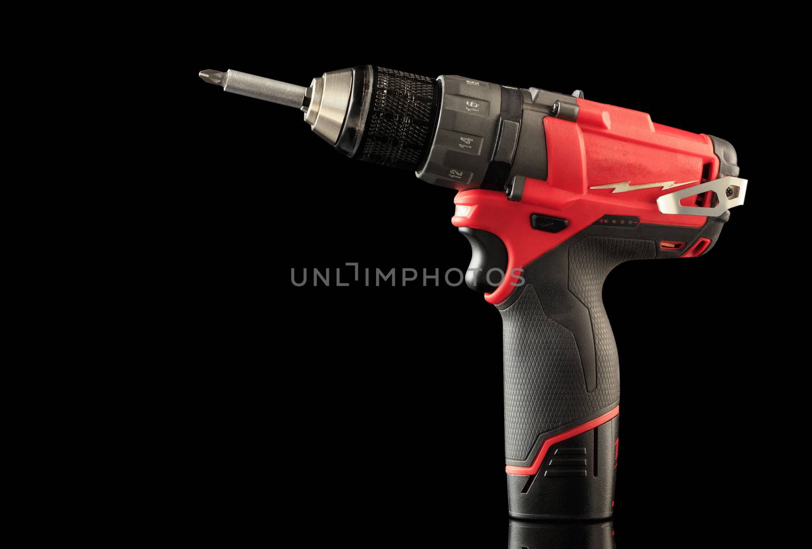 Cordless drill driver in red with rubberized handle in profile, isolated on black background with reflection