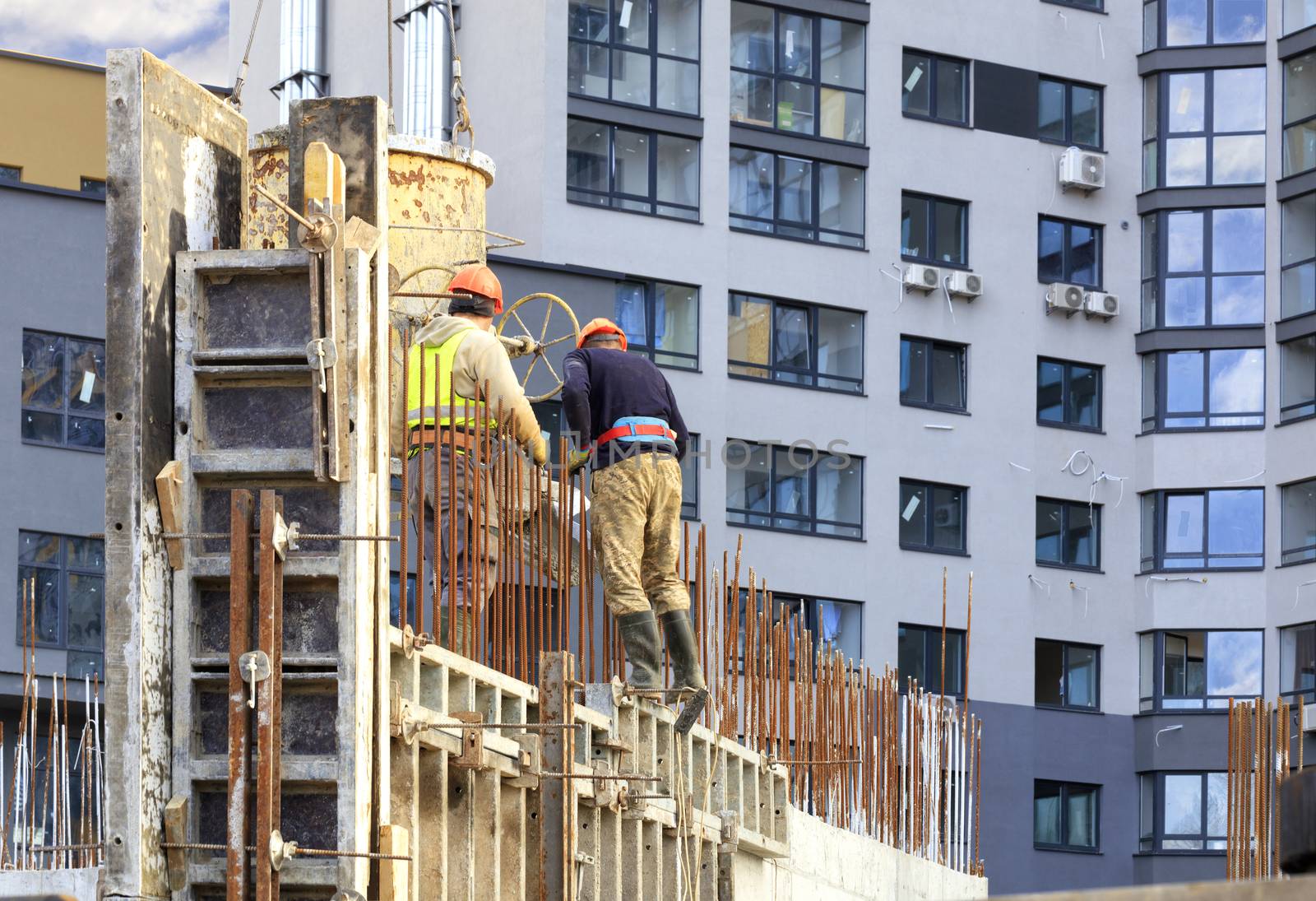 Workers poured concrete in the formwork of the walls on the construction of the new house against the background of a modern residential building.
