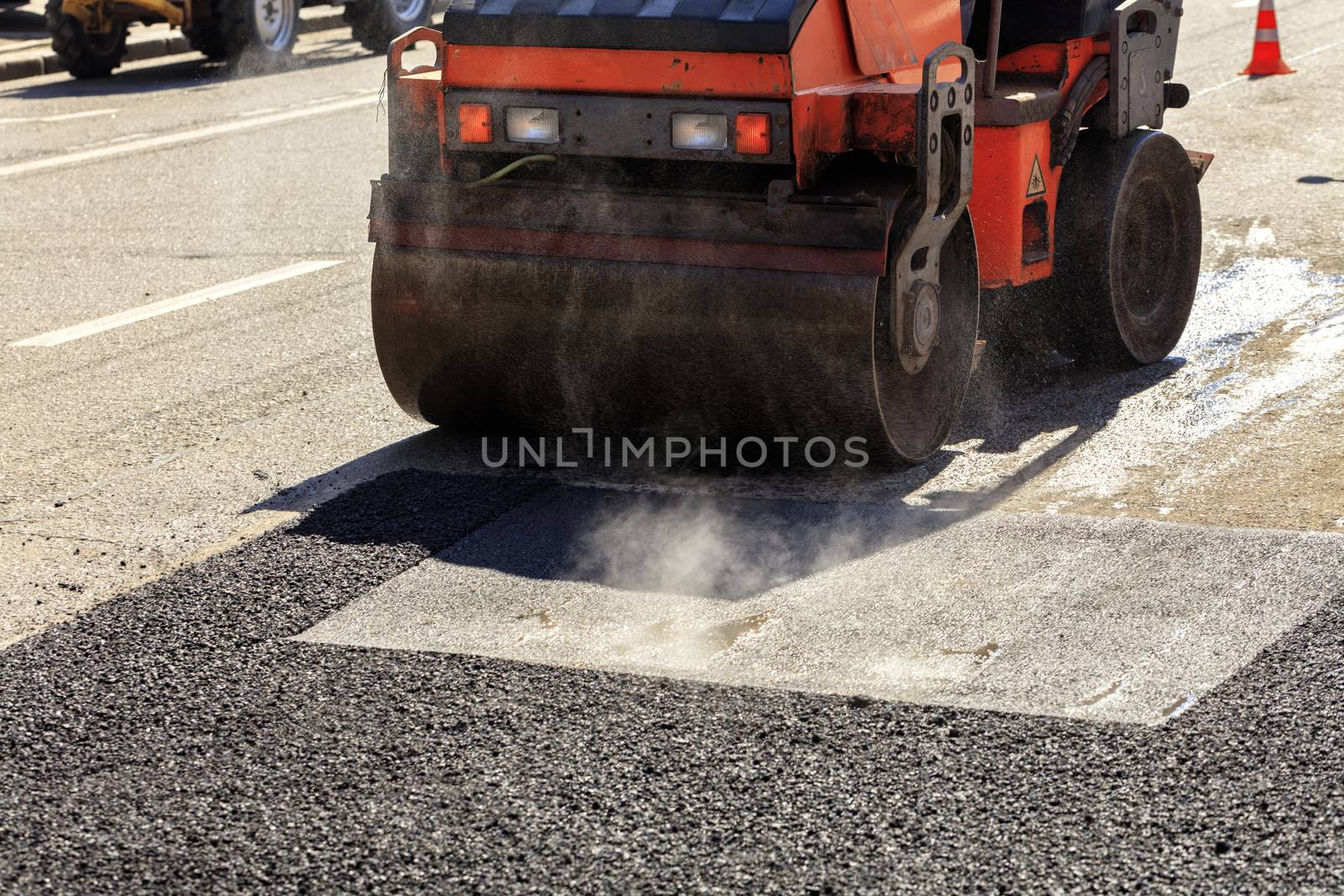 A heavy vibratory road roller compacts asphalt on the road to be repaired. by Sergii