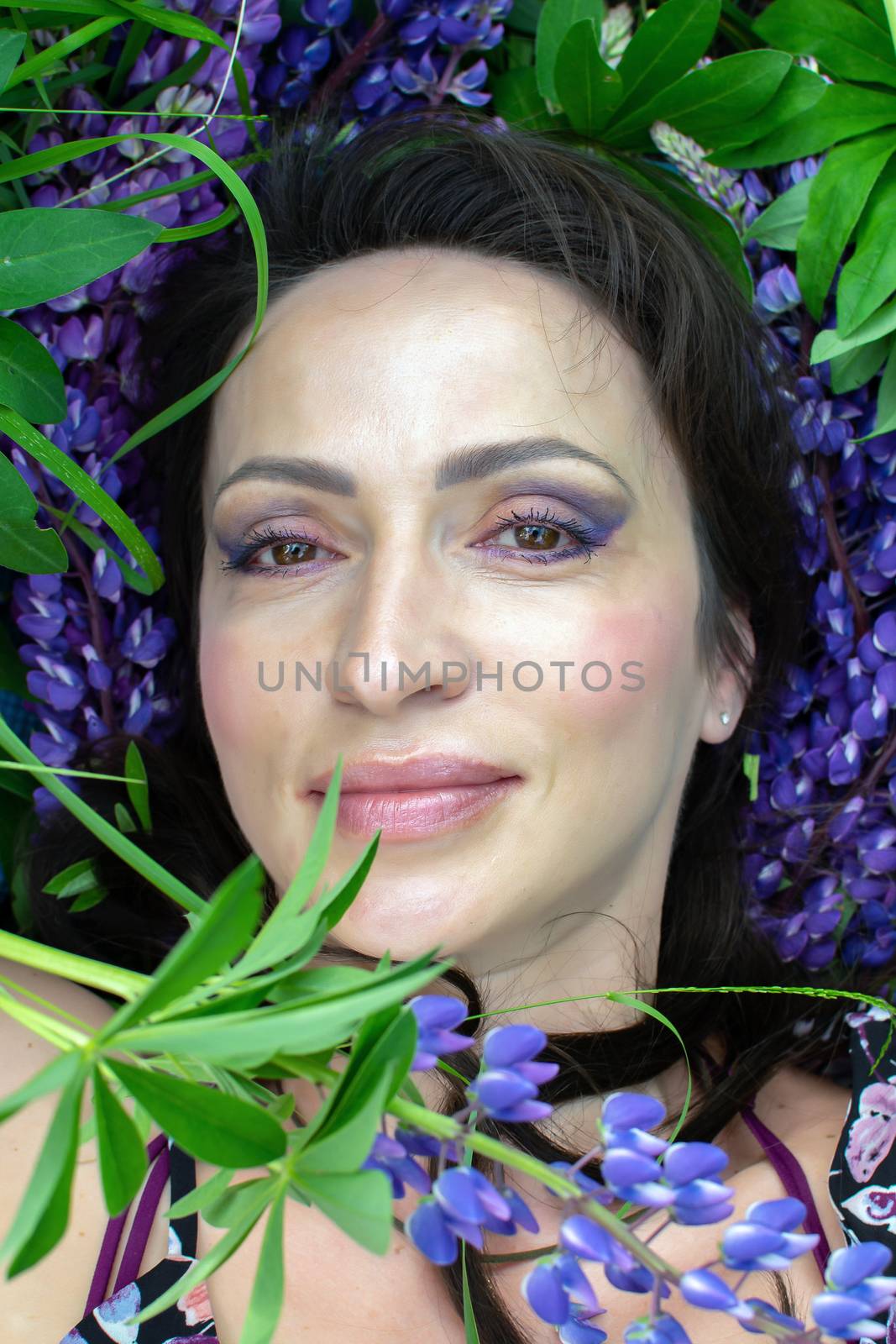 A beautiful woman is relaxing in nature among blooming purple lupines on a Sunny summer day