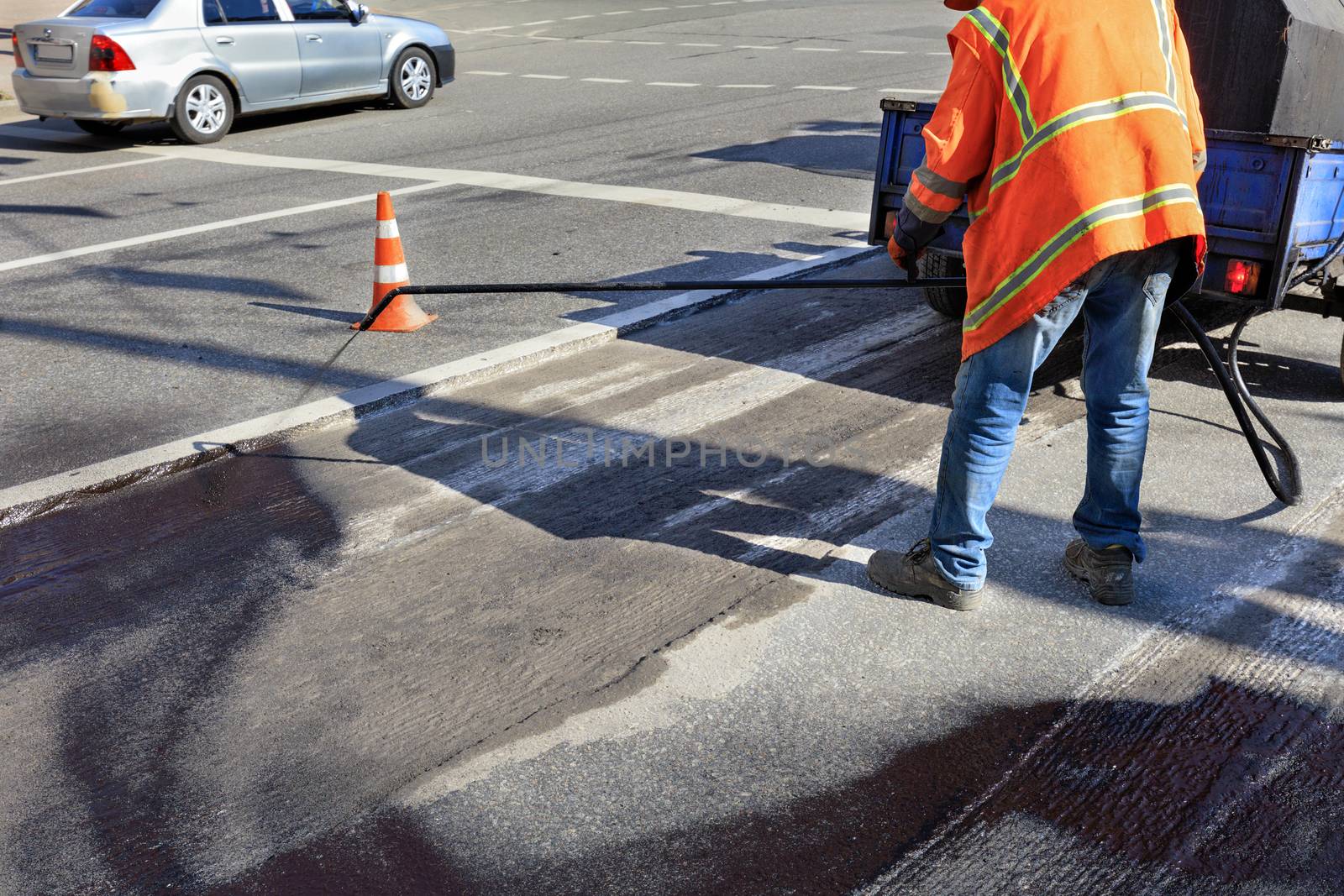The worker sprays bitumen on the asphalt surface. Partial repair of the asphalt road. by Sergii