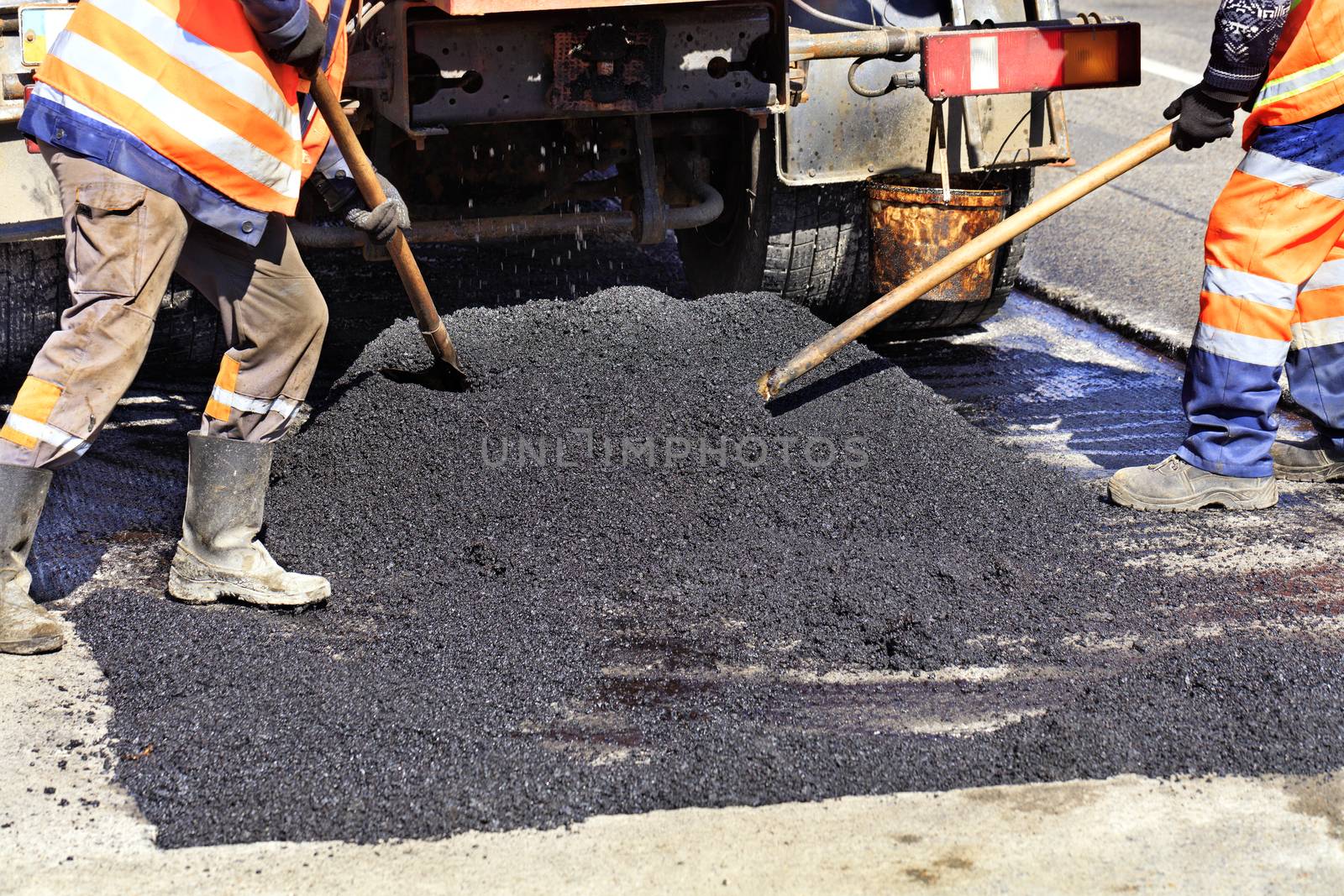The road workers' working group updates the part of the road with fresh hot asphalt with shovels and distributes it evenly over the surface.