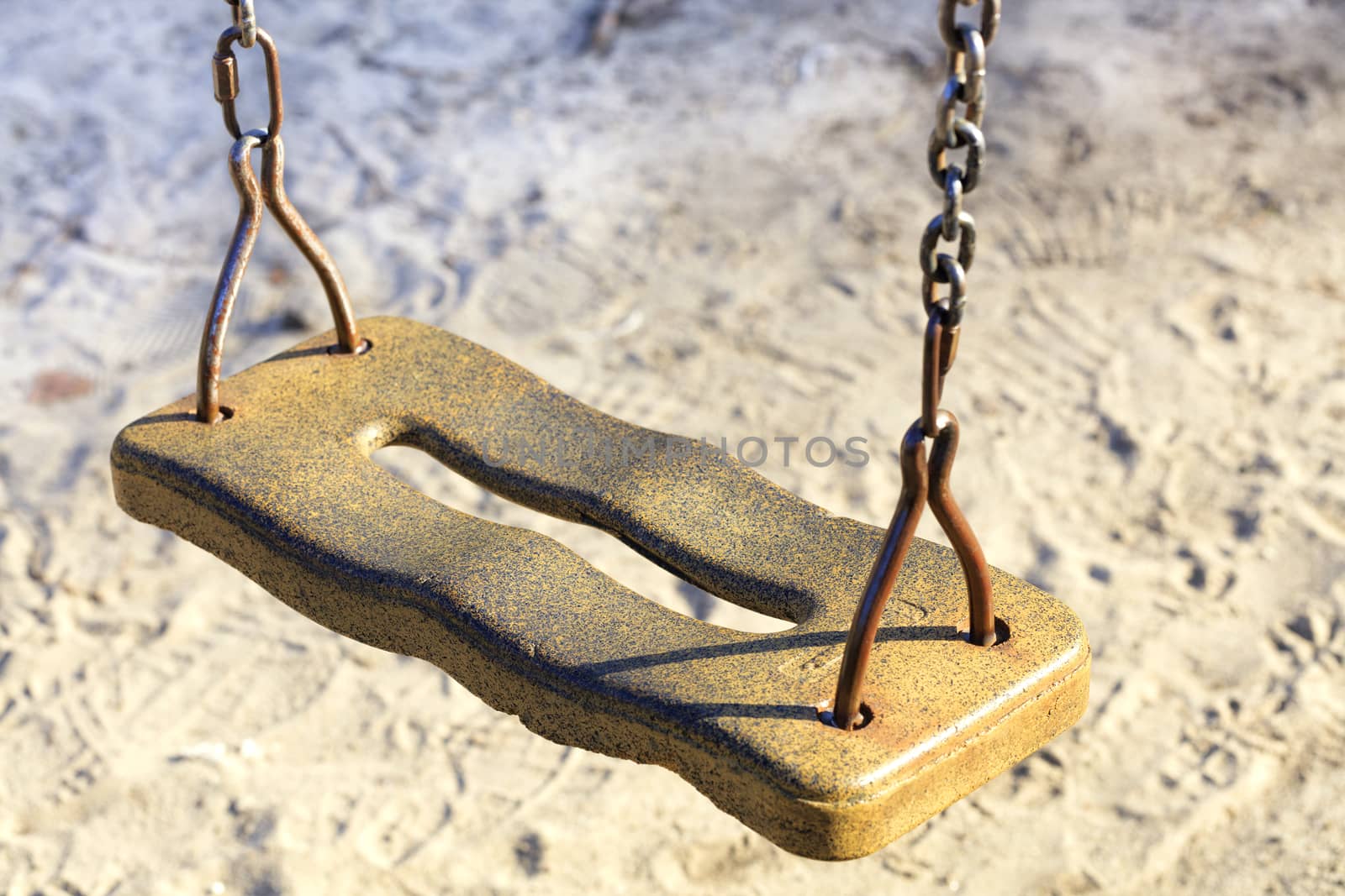 The seat of the old children's swing on a metal chain against the background of worn light sand
