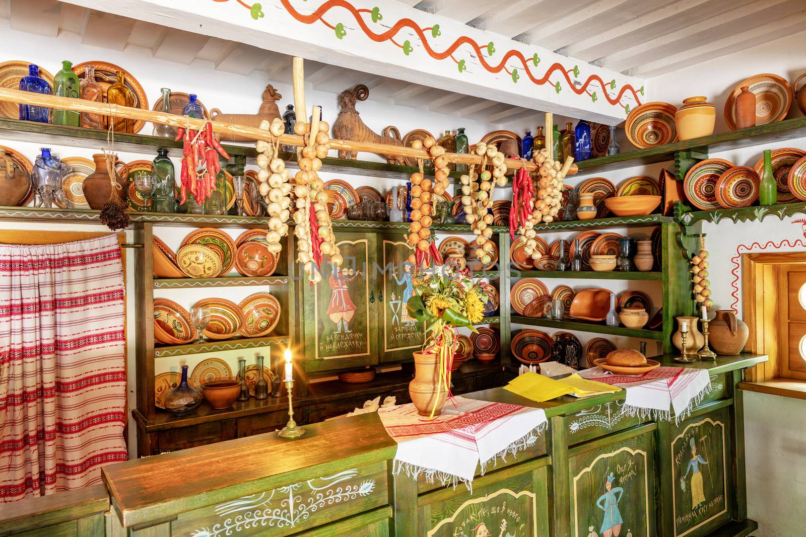 Ceramic painted bowls, plates and jugs on a wooden shelf on the wall, an old counter with glassware in the interior of an old Ukrainian rural cafe and shop.