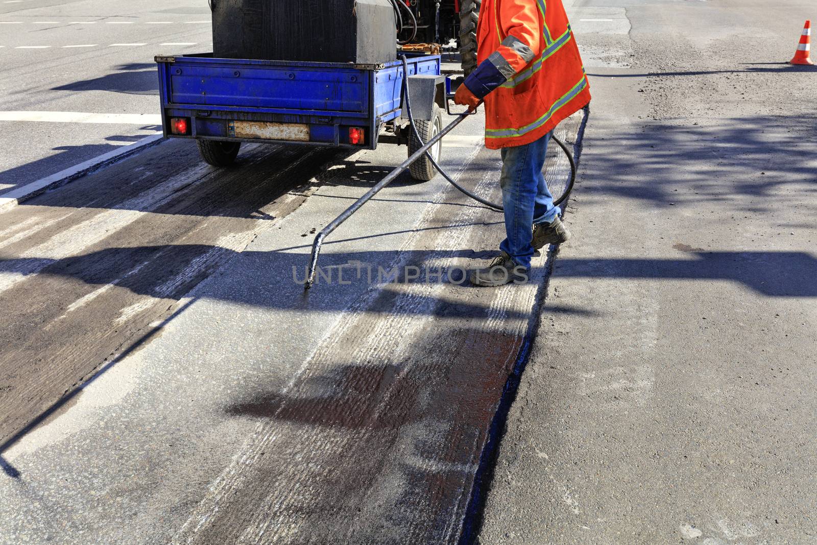 Worker repairs part of the asphalt road, spraying bitumen on the asphalt surface. by Sergii