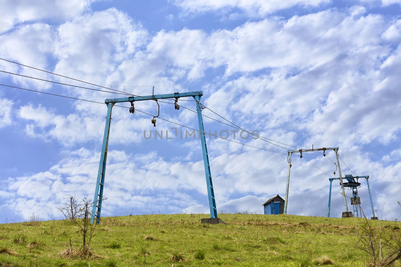 The frame of the mountain cable lift stands apart on the top of the mountain against the background of a deep blue sky with white clouds in the Carpathians.