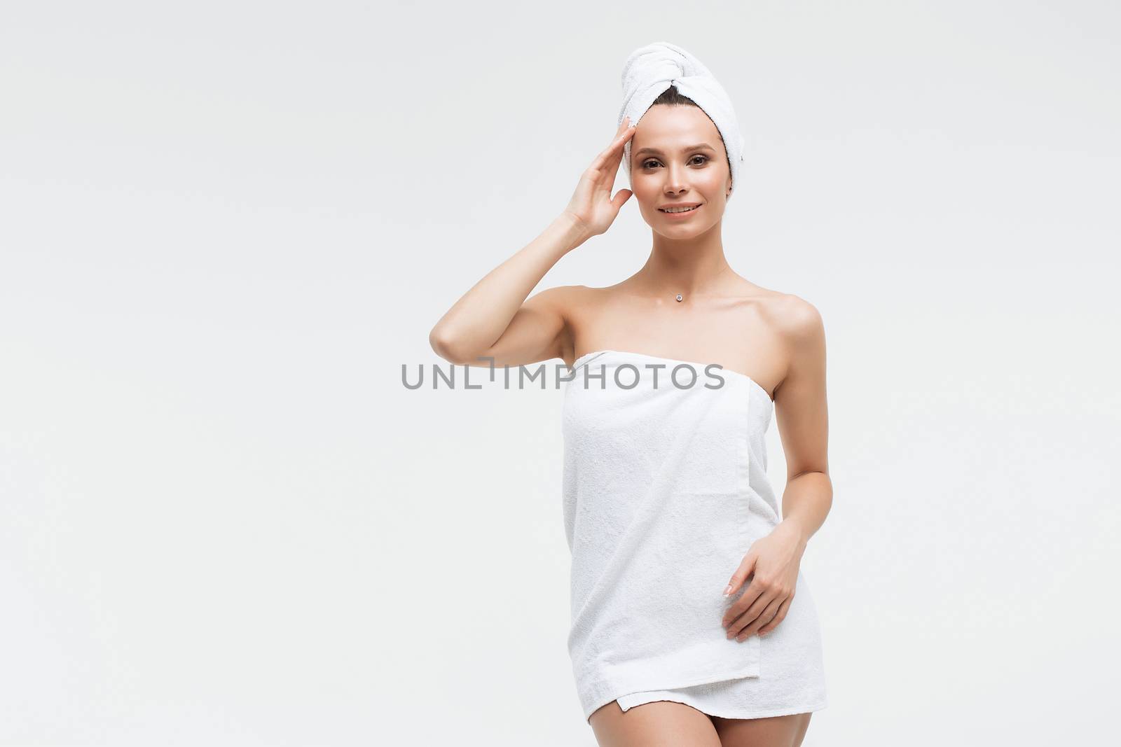 Sensual woman in fluffy white towel on head looking at finger touching towel on body