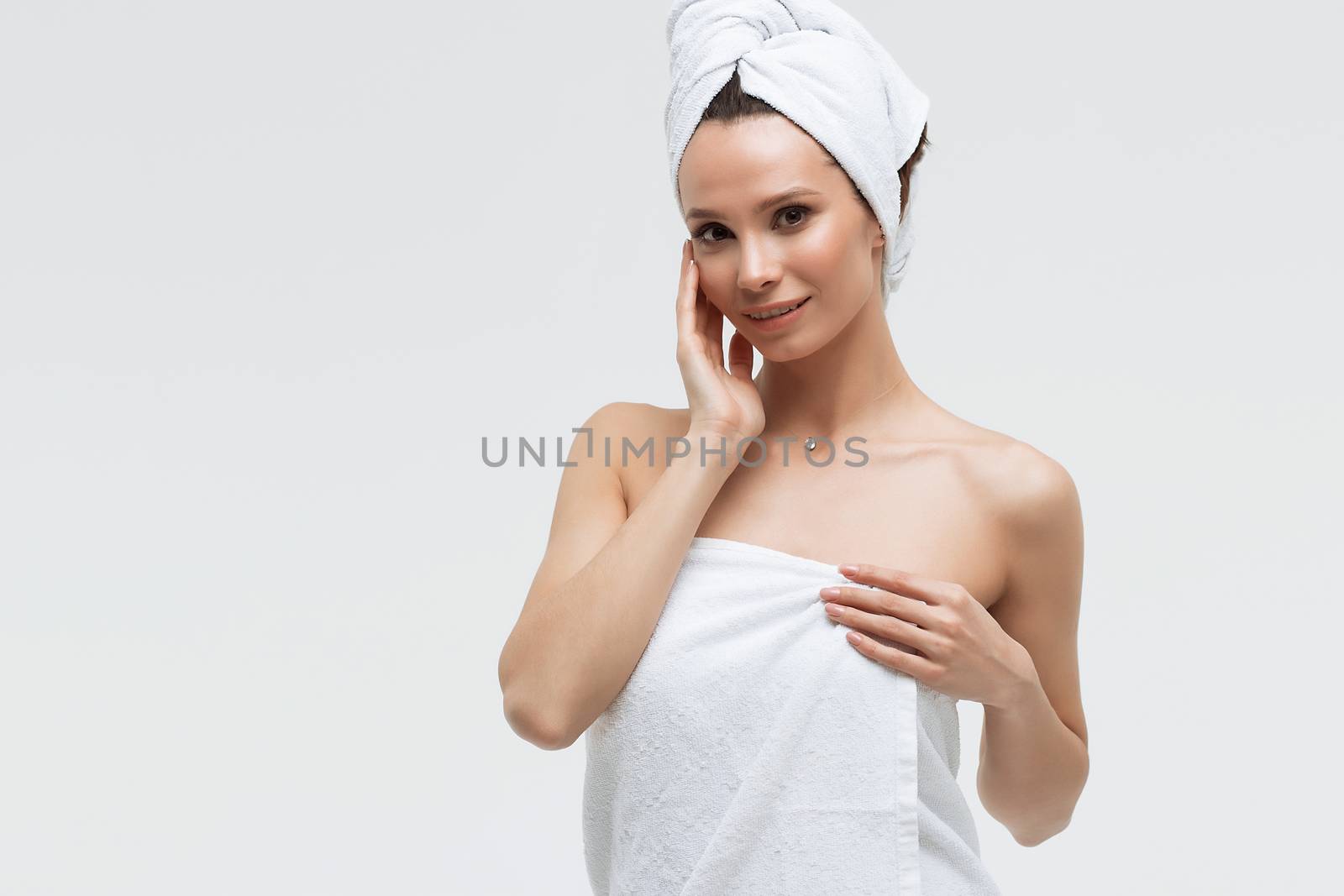 Sensual woman in fluffy white towel on head looking at finger touching towel on body