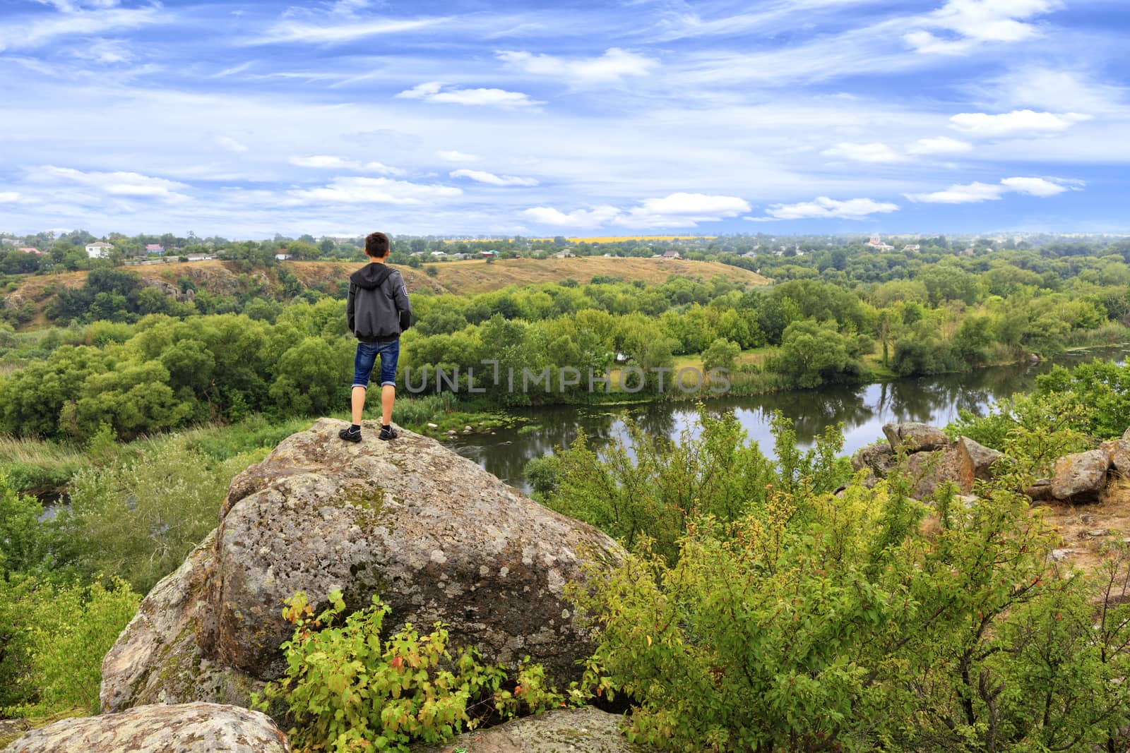 A teenager stands on top of a large stone boulder on the banks of the Southern Bug and looks into the distance. by Sergii