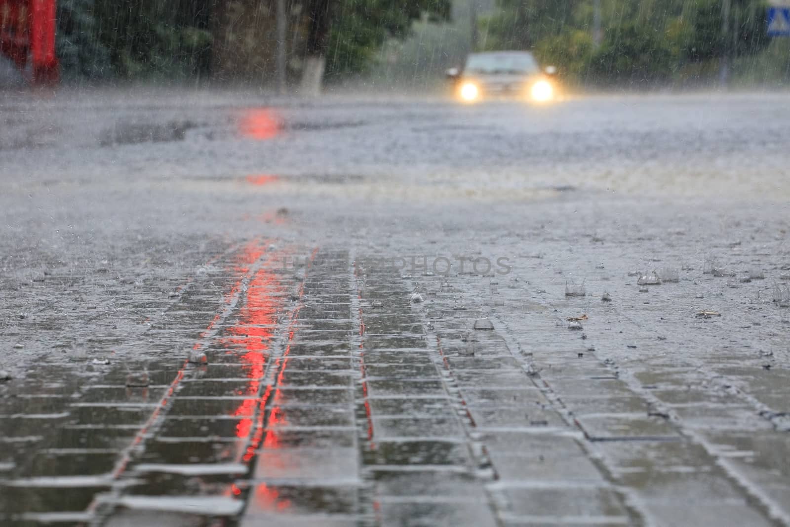 Torrential rain at an empty crossroads and red light reflected in the flow of water on a city street.