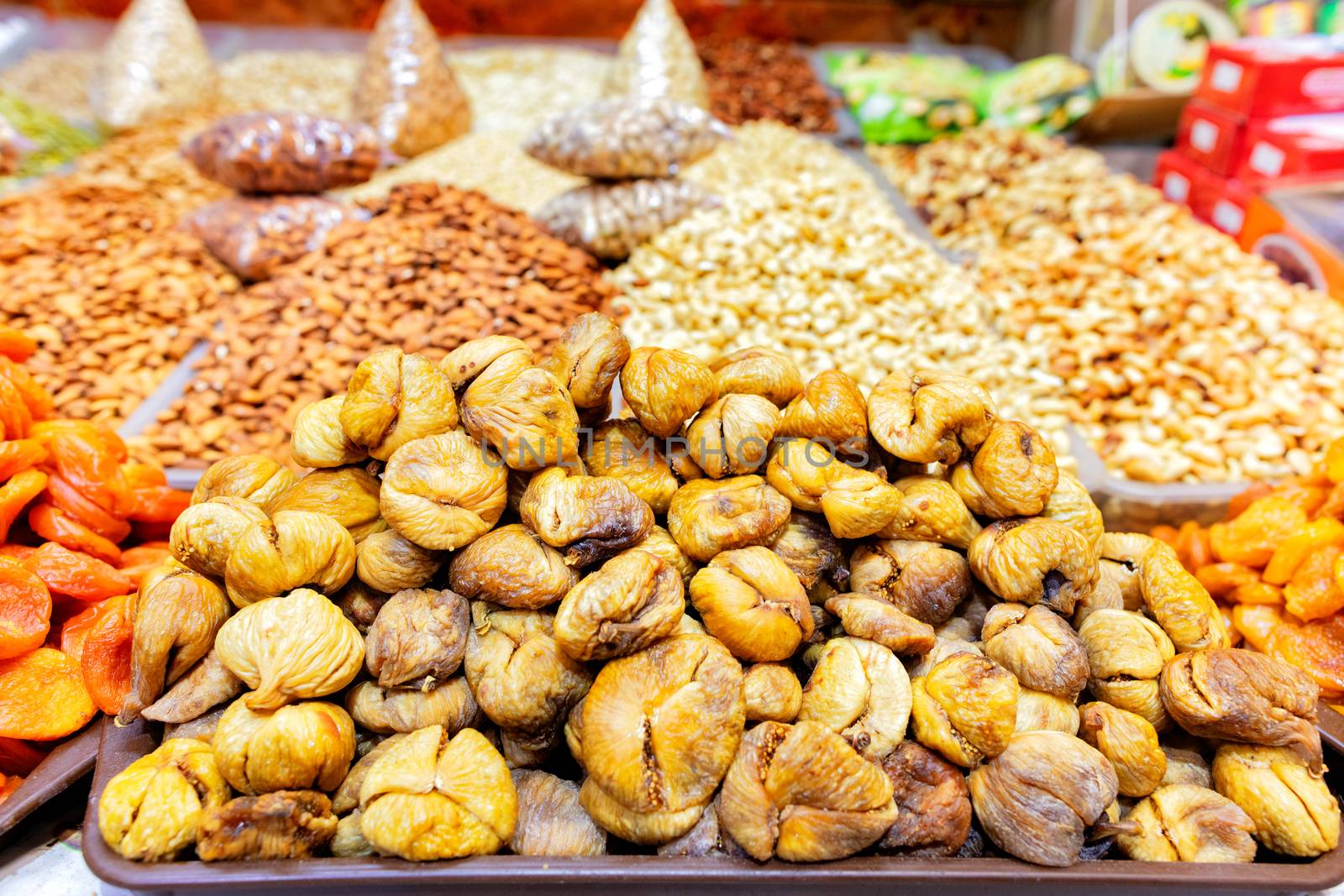 Slides with dried ugly figs, dried apricots on a background of various nuts in blurry form are sold on the shelves of the eastern market.