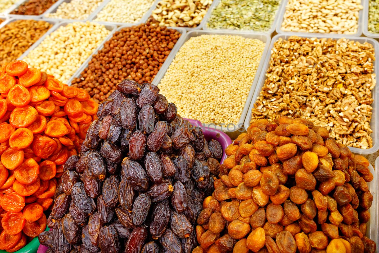 Slides with dates close-up, dried apricots, prunes against the background of various nuts in a blurred are sold form on the shelves of the eastern market.