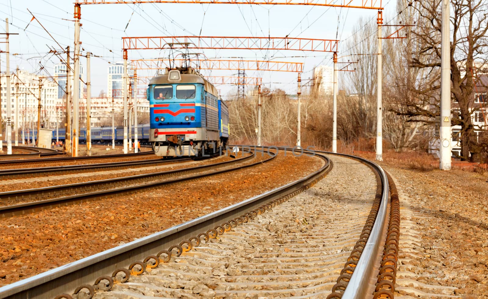 The prospect of a multi-channel railway for electric trains with overhead power lines in the early spring morning, against the backdrop of an urban blurred landscape.
